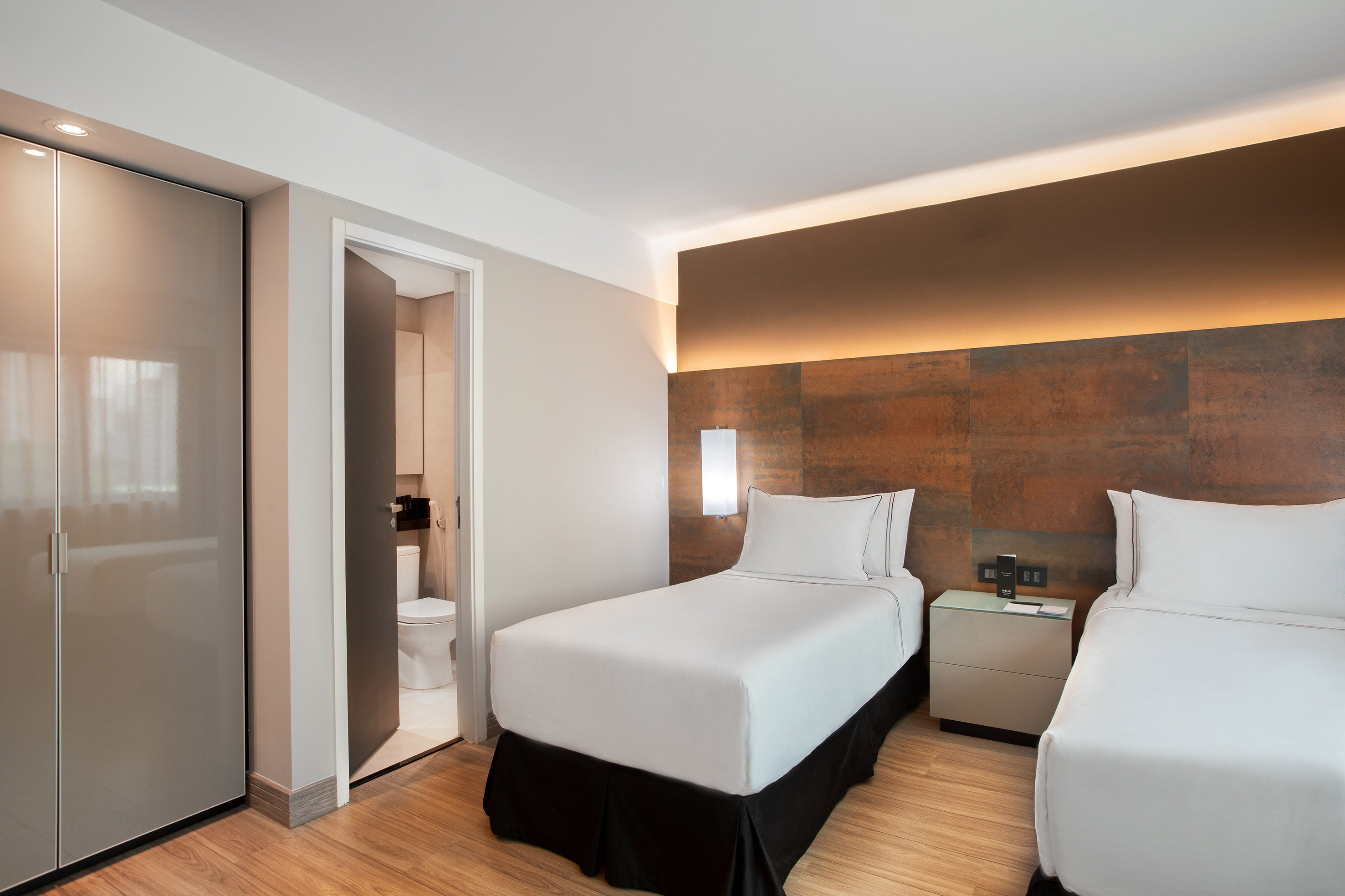 Hotel guest room with two twin beds, modern decor, wood floor.
