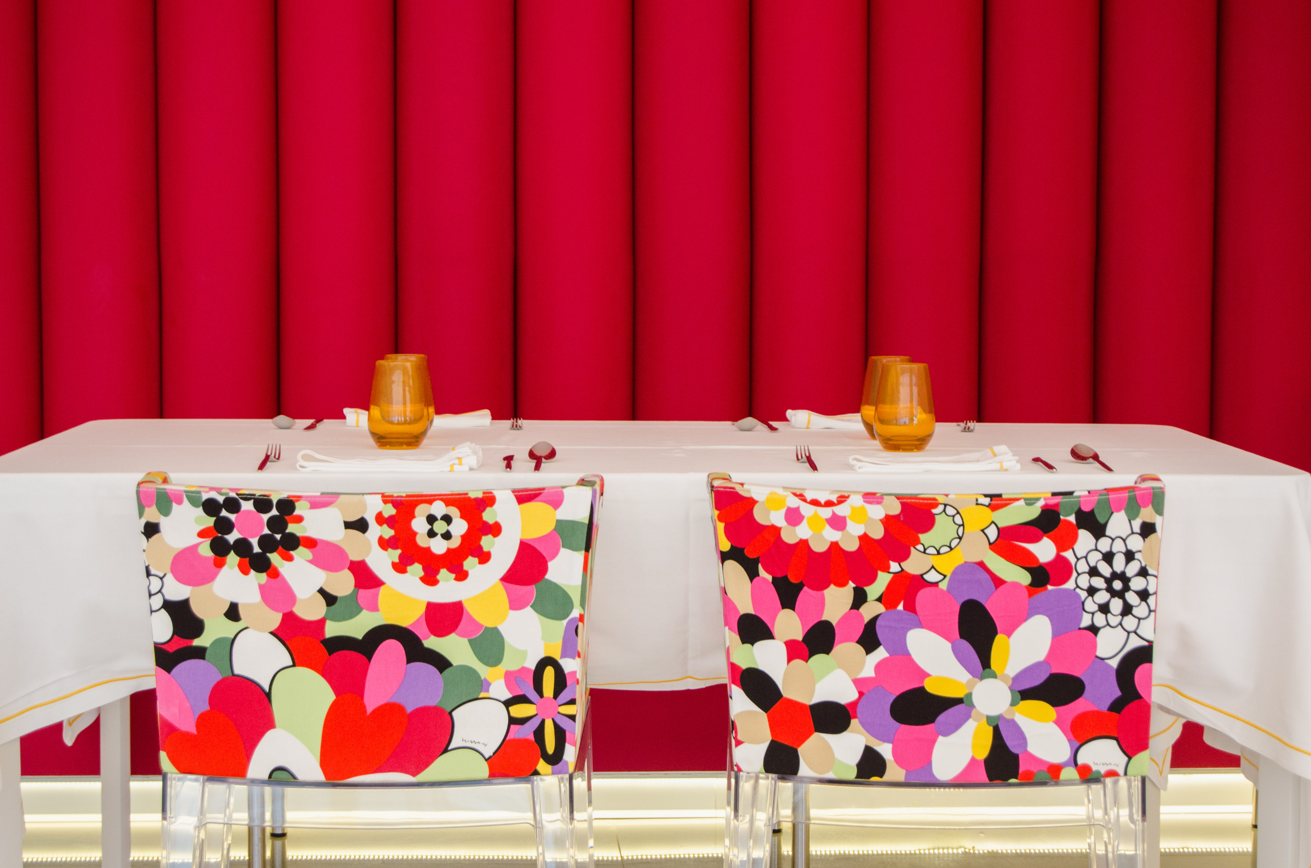Vibrant floral chairs and set table against a bold red background.