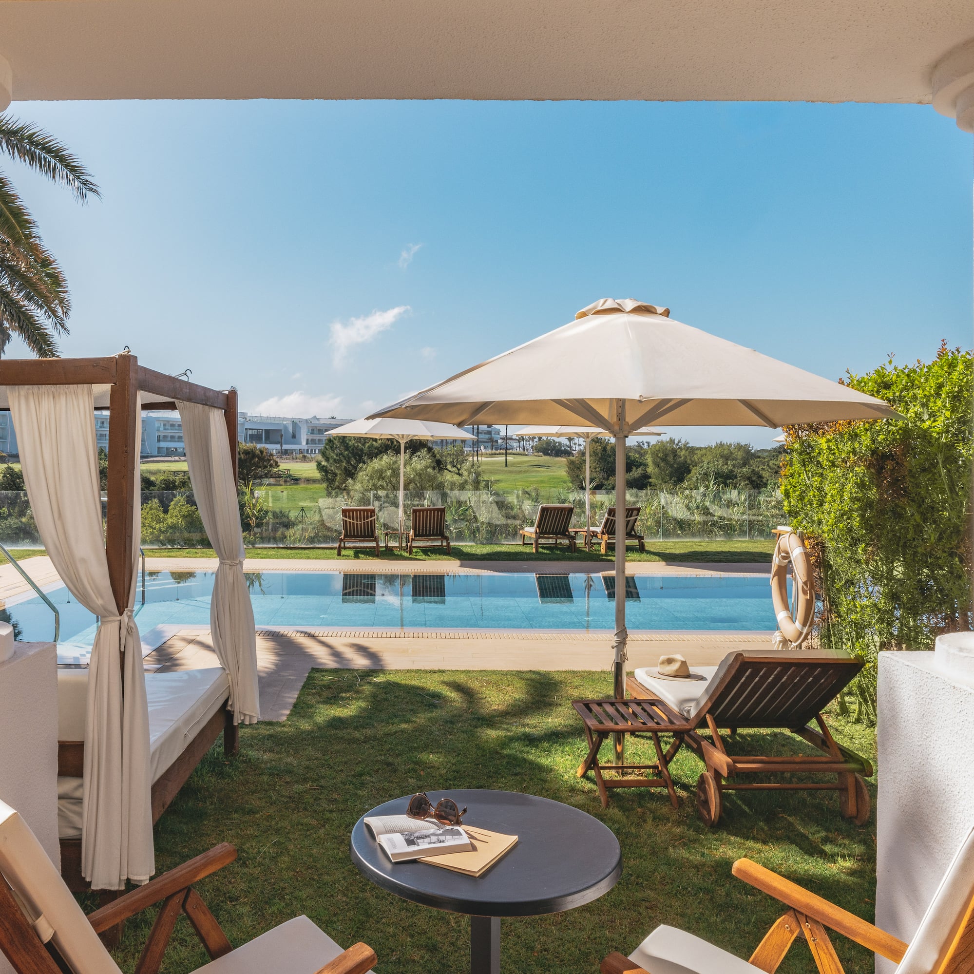Hotel patio with swimming pool, daybed, sun loungers, and golf course view.