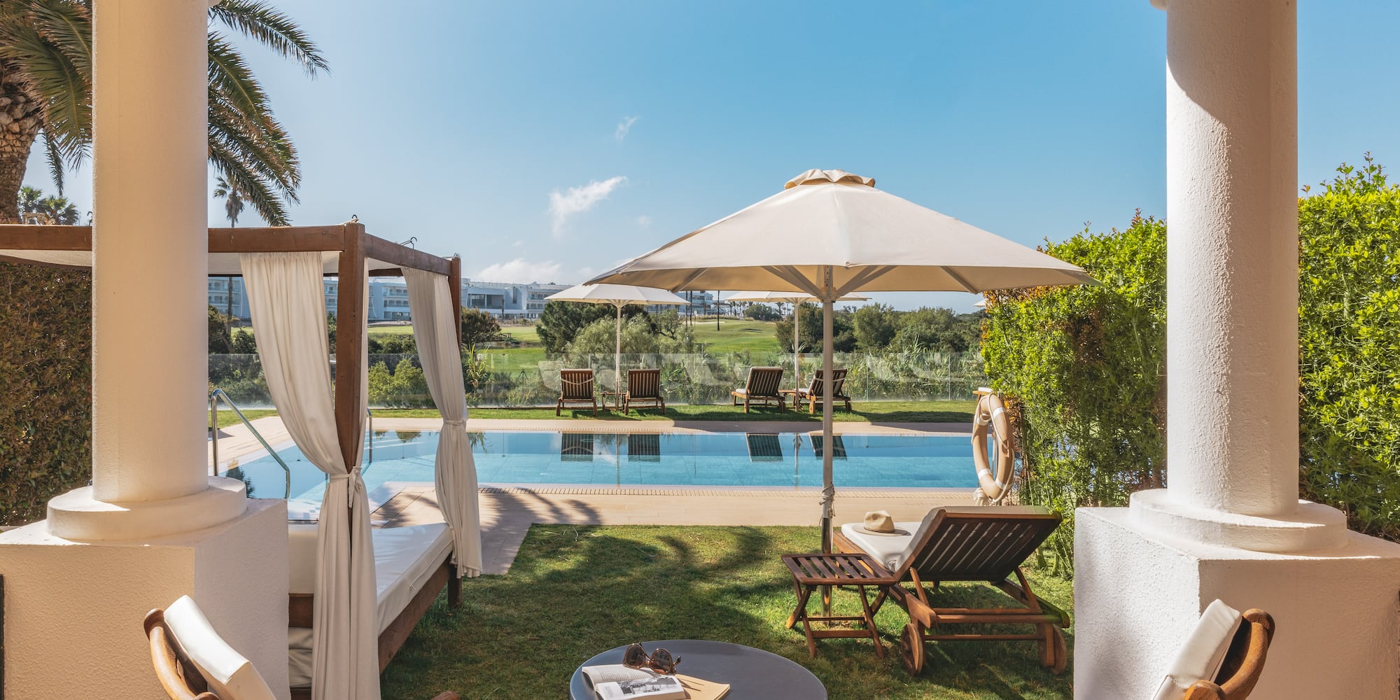 Hotel patio with swimming pool, daybed, sun loungers, and golf course view.