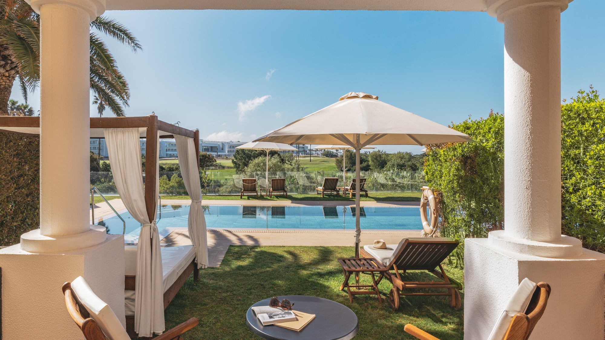 Hotel patio with swimming pool, daybed, sun loungers, and golf course view.