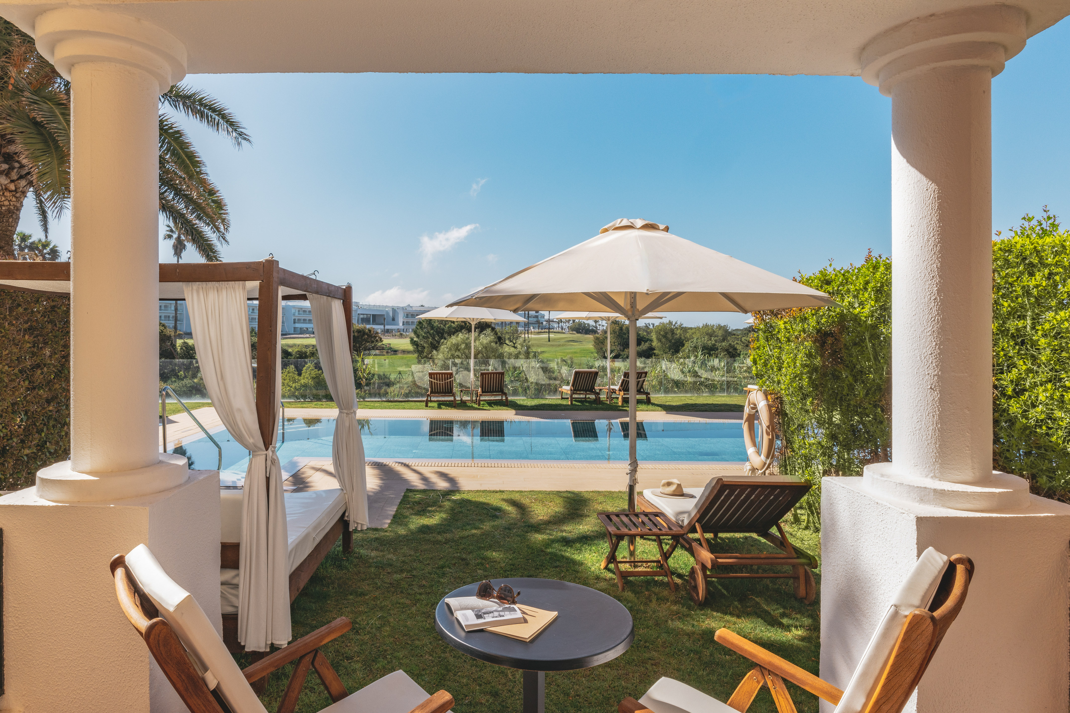 Hotel patio with swimming pool, daybed, sun loungers, and golf course view.