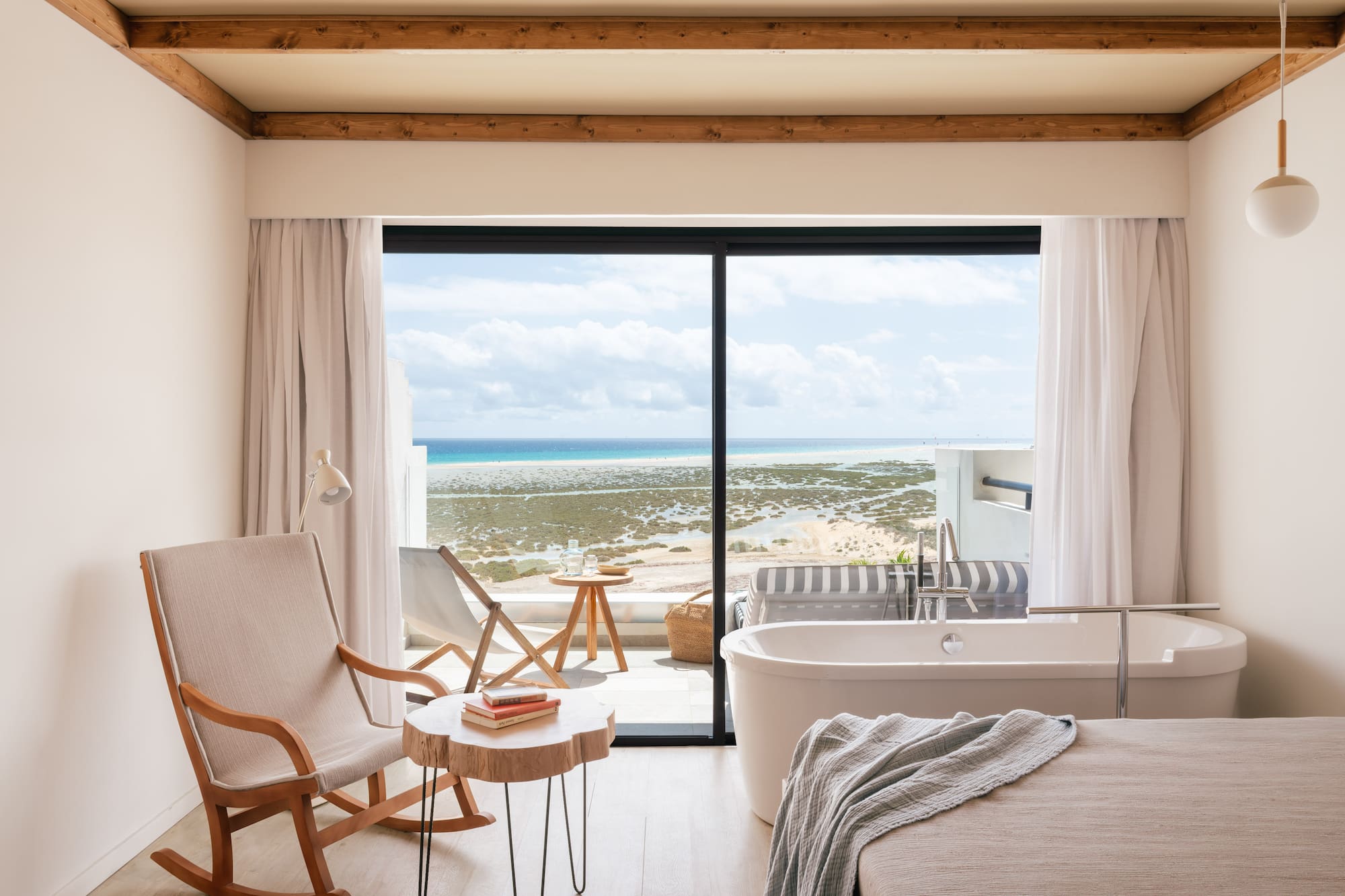 Habitación moderna con vistas al mar, bañera junto al ventanal y mecedora de madera.