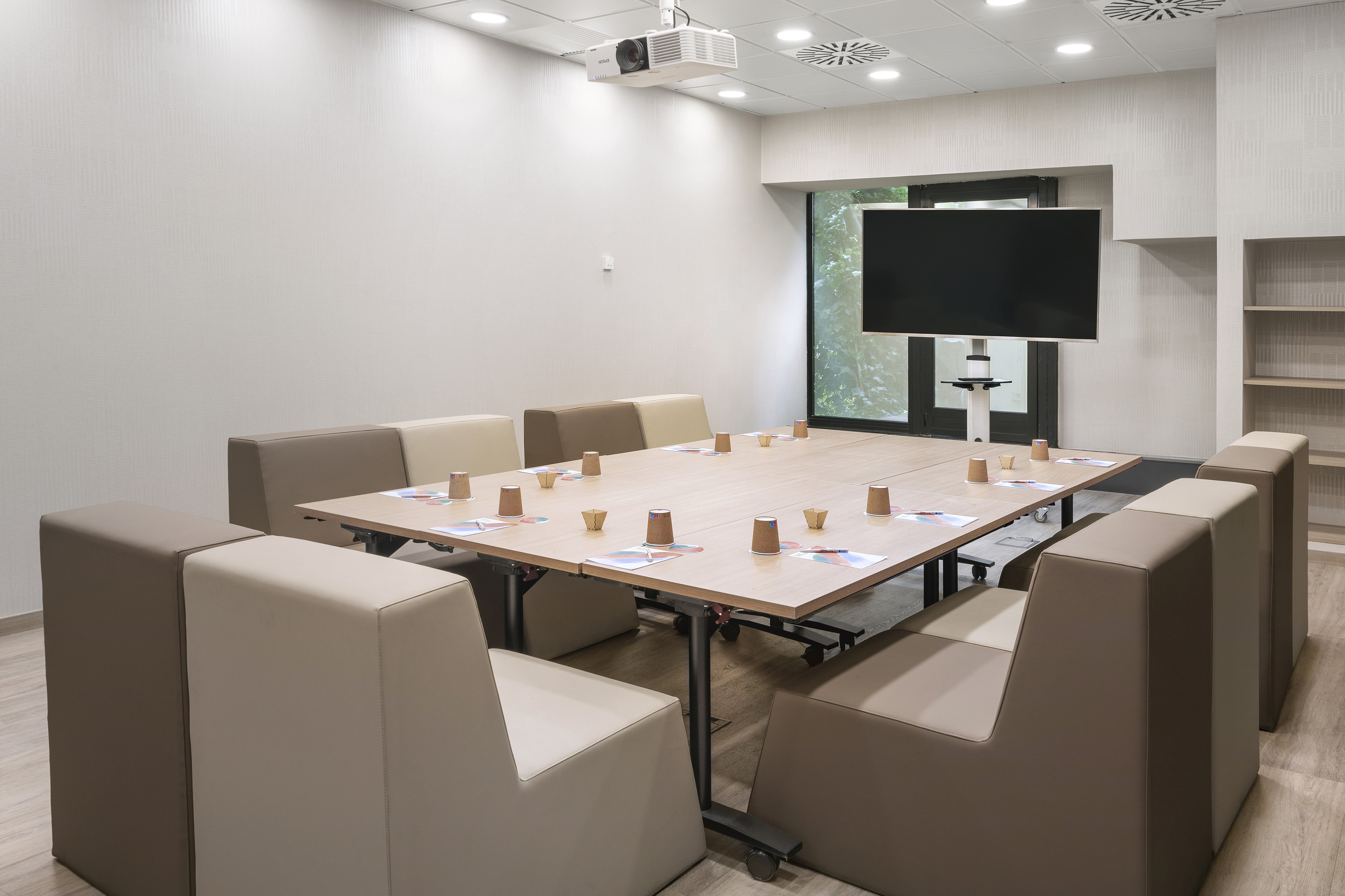Contemporary conference room with wooden table, modular seats, projector, TV.