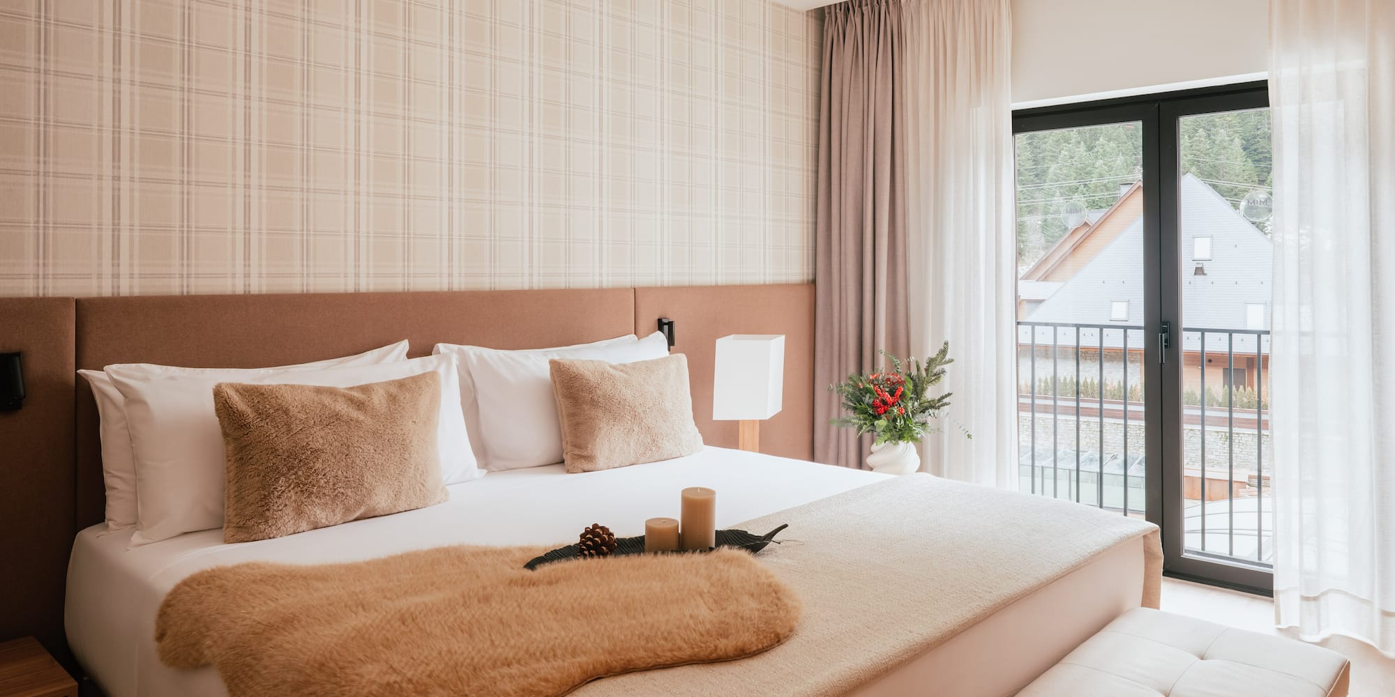 Cozy hotel bedroom with neutral decor, fur throw, plaid wall, and balcony view.