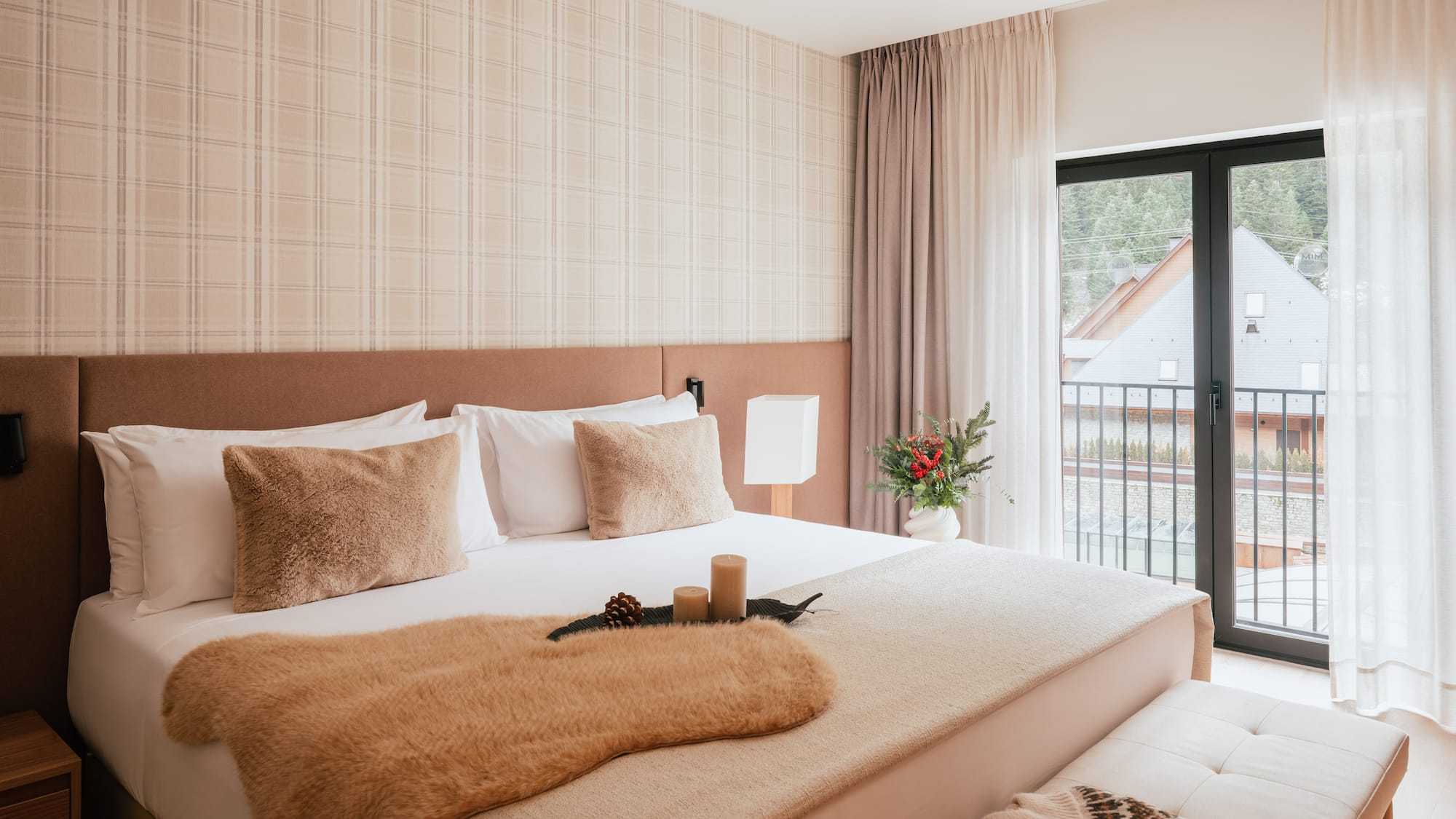 Cozy hotel bedroom with neutral decor, fur throw, plaid wall, and balcony view.
