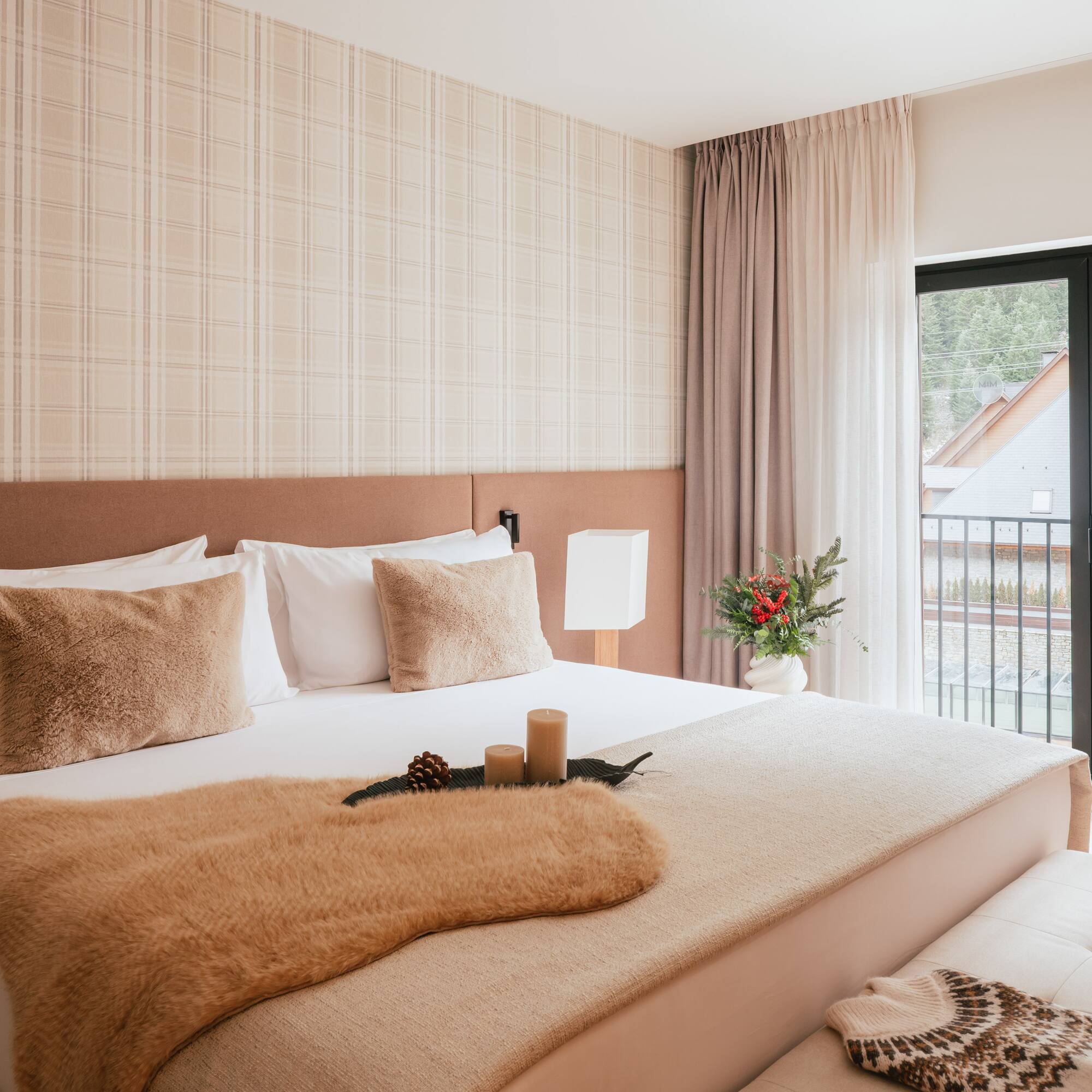 Cozy hotel bedroom with neutral decor, fur throw, plaid wall, and balcony view.
