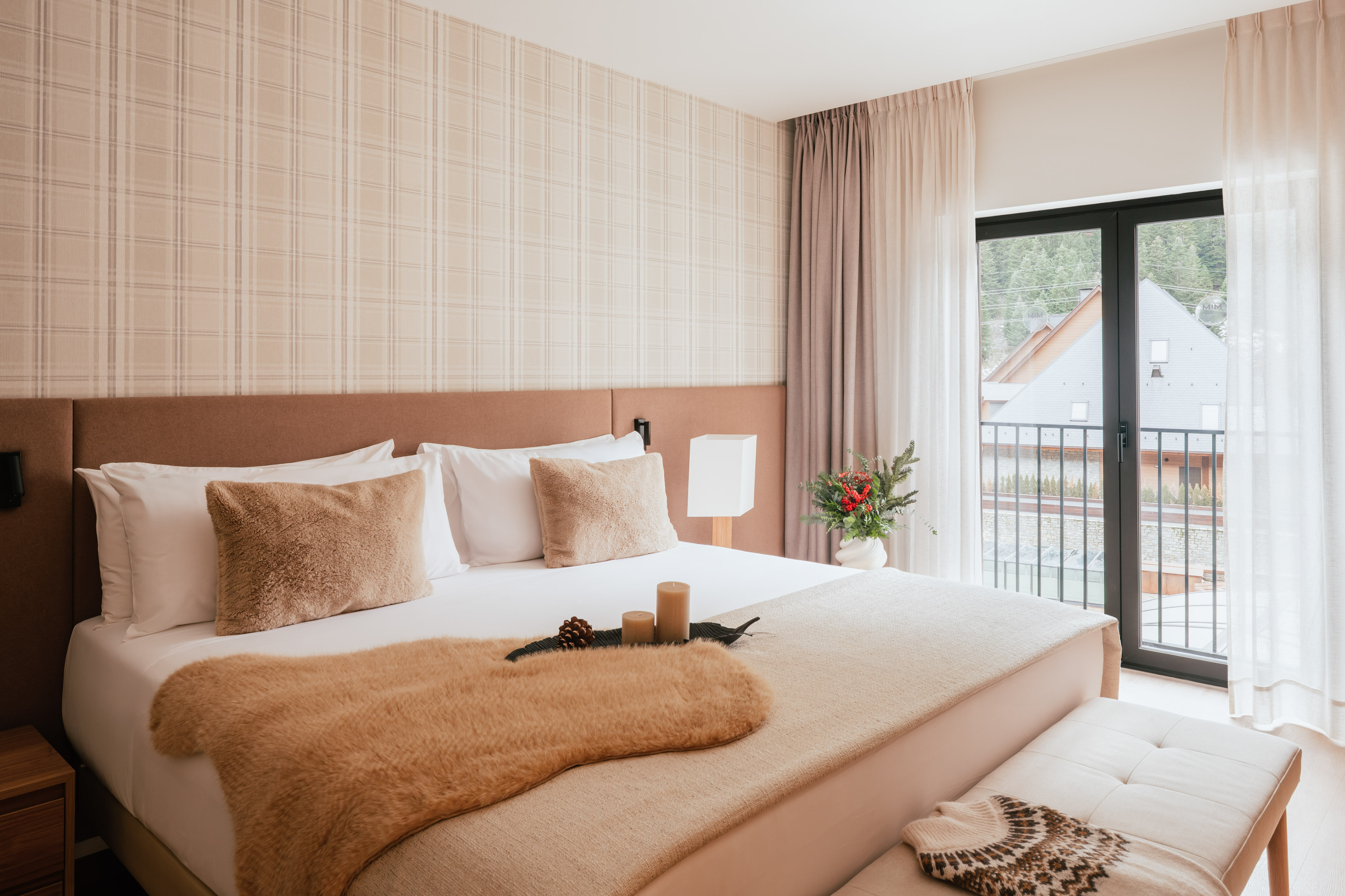 Cozy hotel bedroom with neutral decor, fur throw, plaid wall, and balcony view.