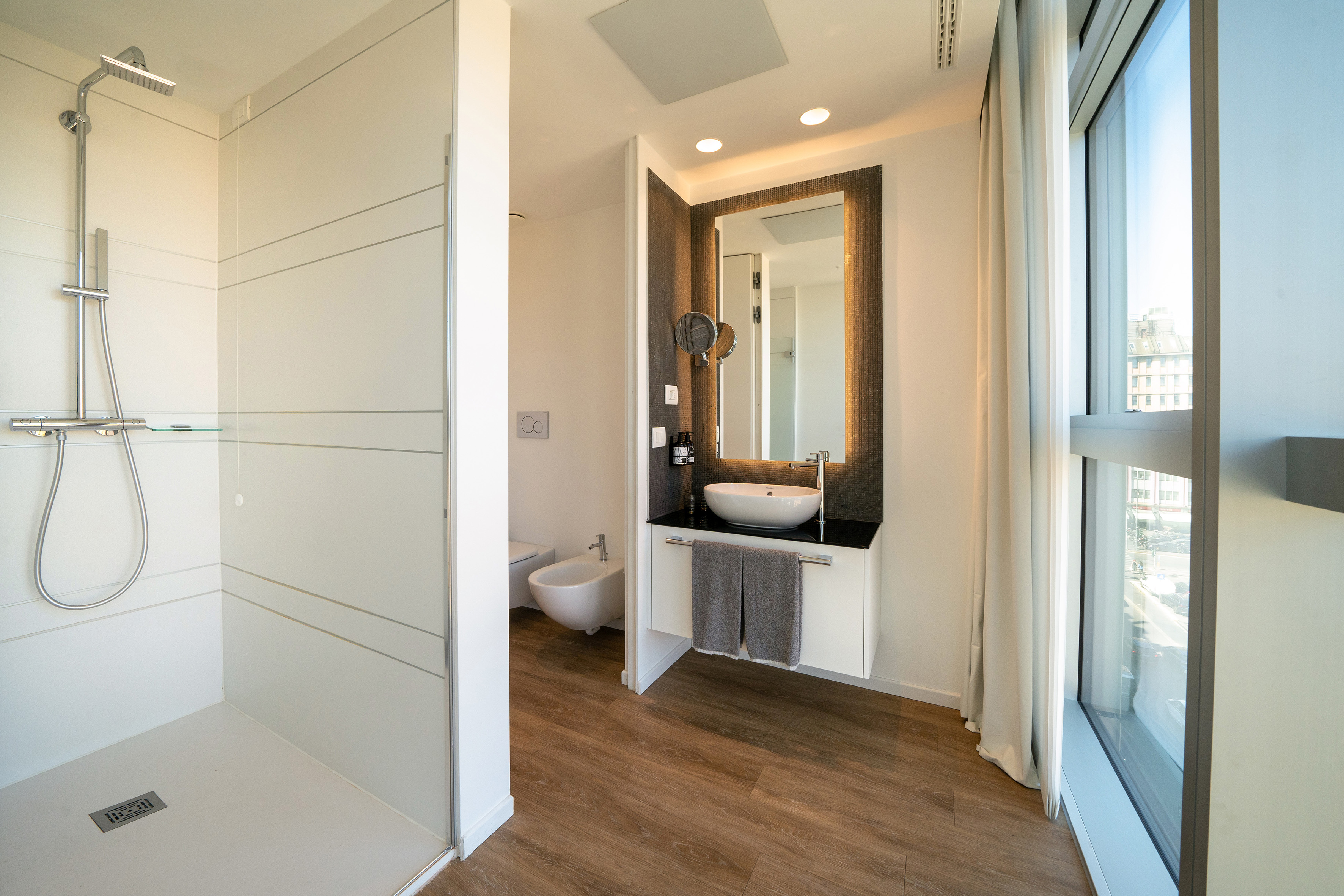Modern bathroom: walk-in shower, vessel sink vanity, backlit mirror, wood floor.