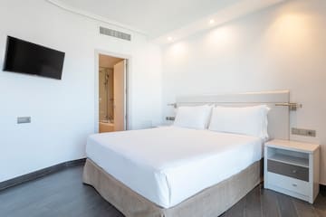 a bed with white sheets and a tv on the wall