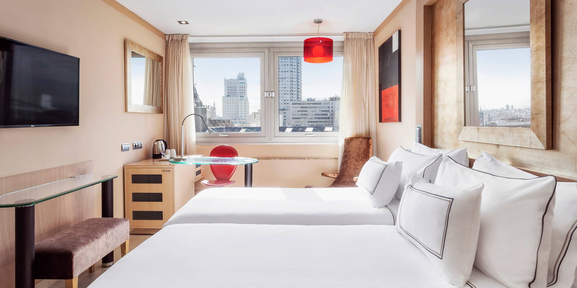 Modern hotel room with twin beds, city view, TV, and red accents.