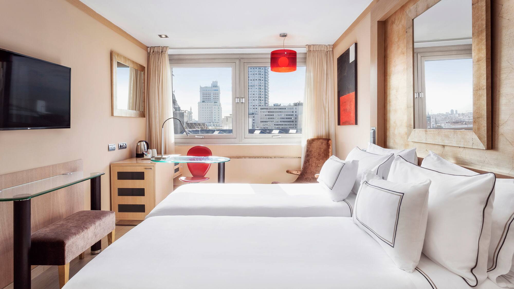 Modern hotel room with twin beds, city view, TV, and red accents.