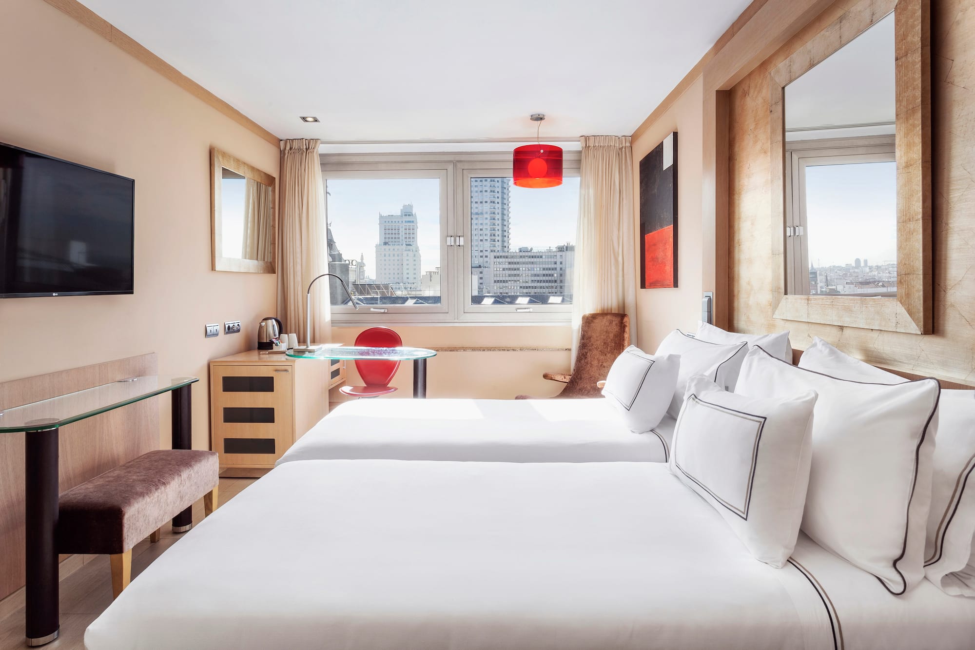 Modern hotel room with twin beds, city view, TV, and red accents.