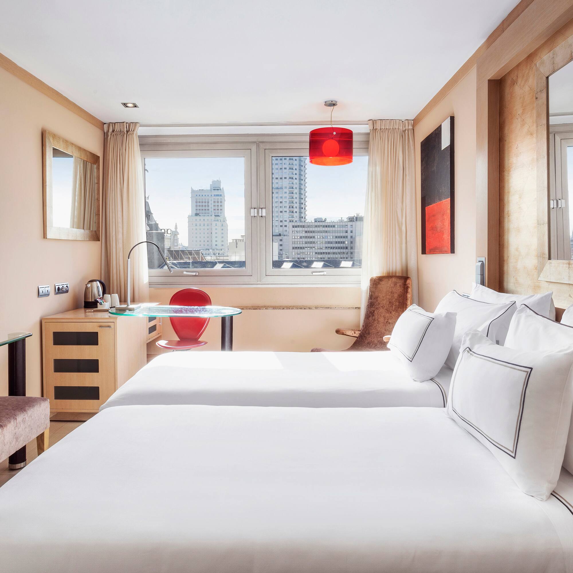 Modern hotel room with twin beds, city view, TV, and red accents.