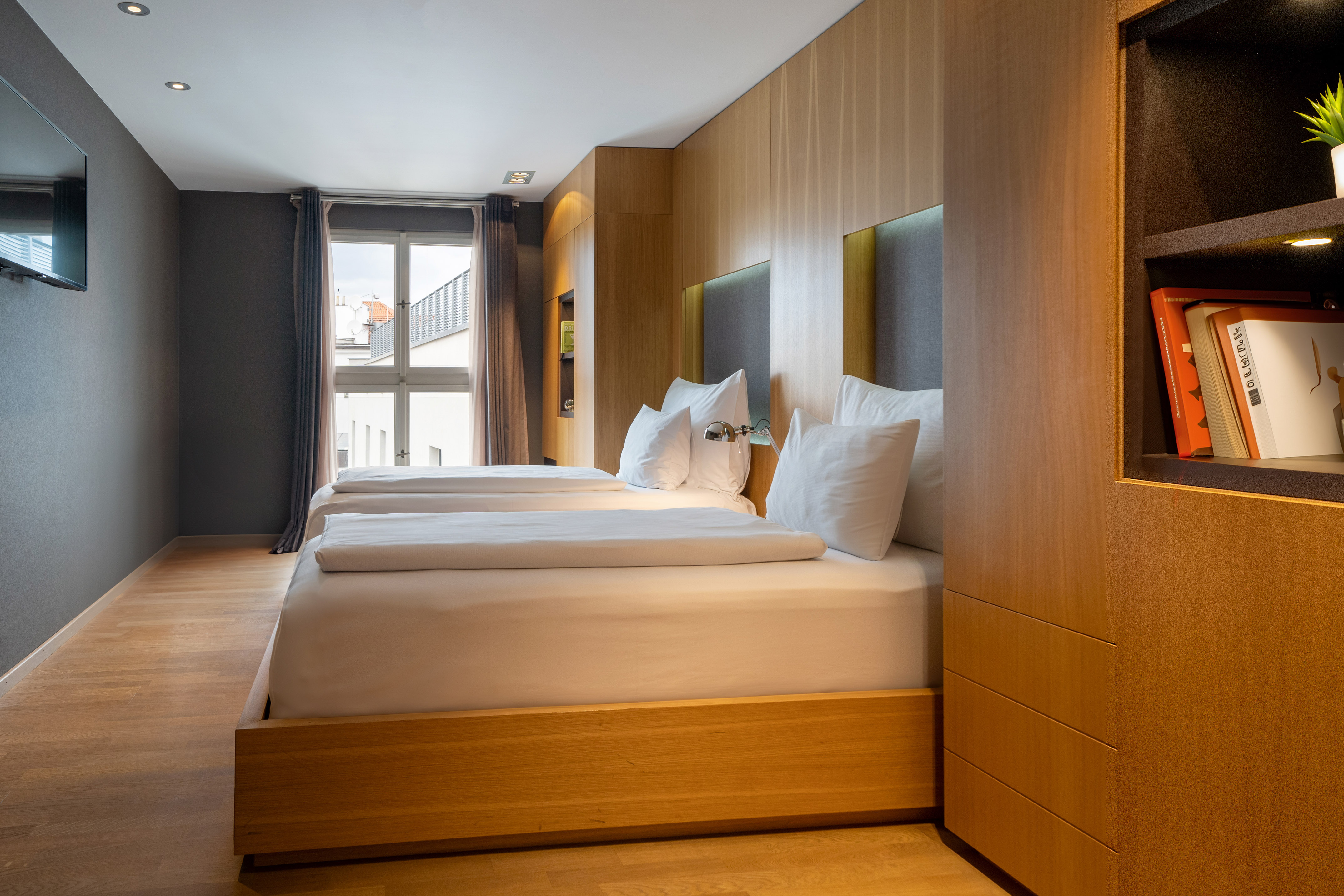 Modern hotel room with twin beds, sleek wood paneling, and a bright window.