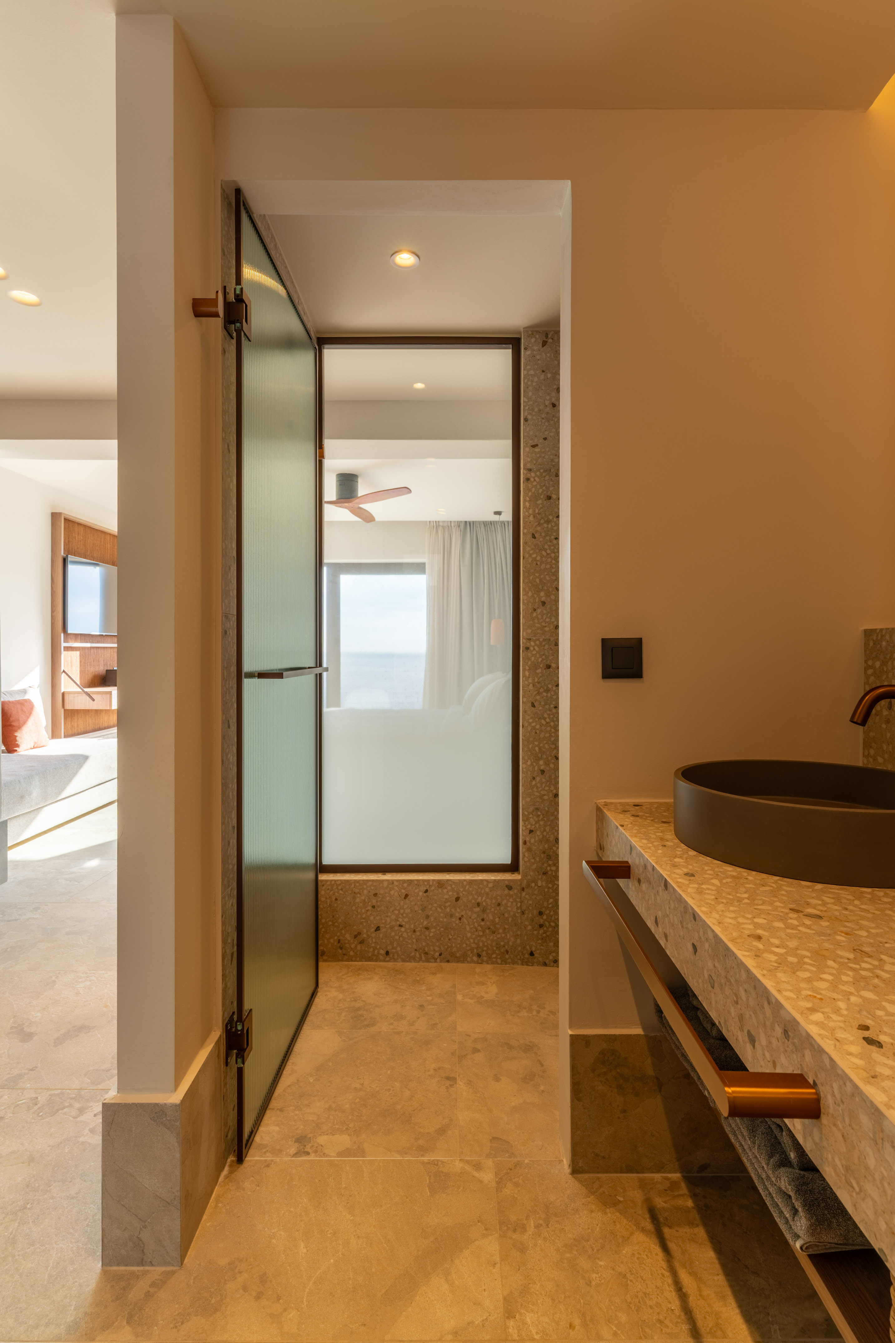 Modern bathroom vanity, dark sink, fluted glass door to ocean-view bedroom.