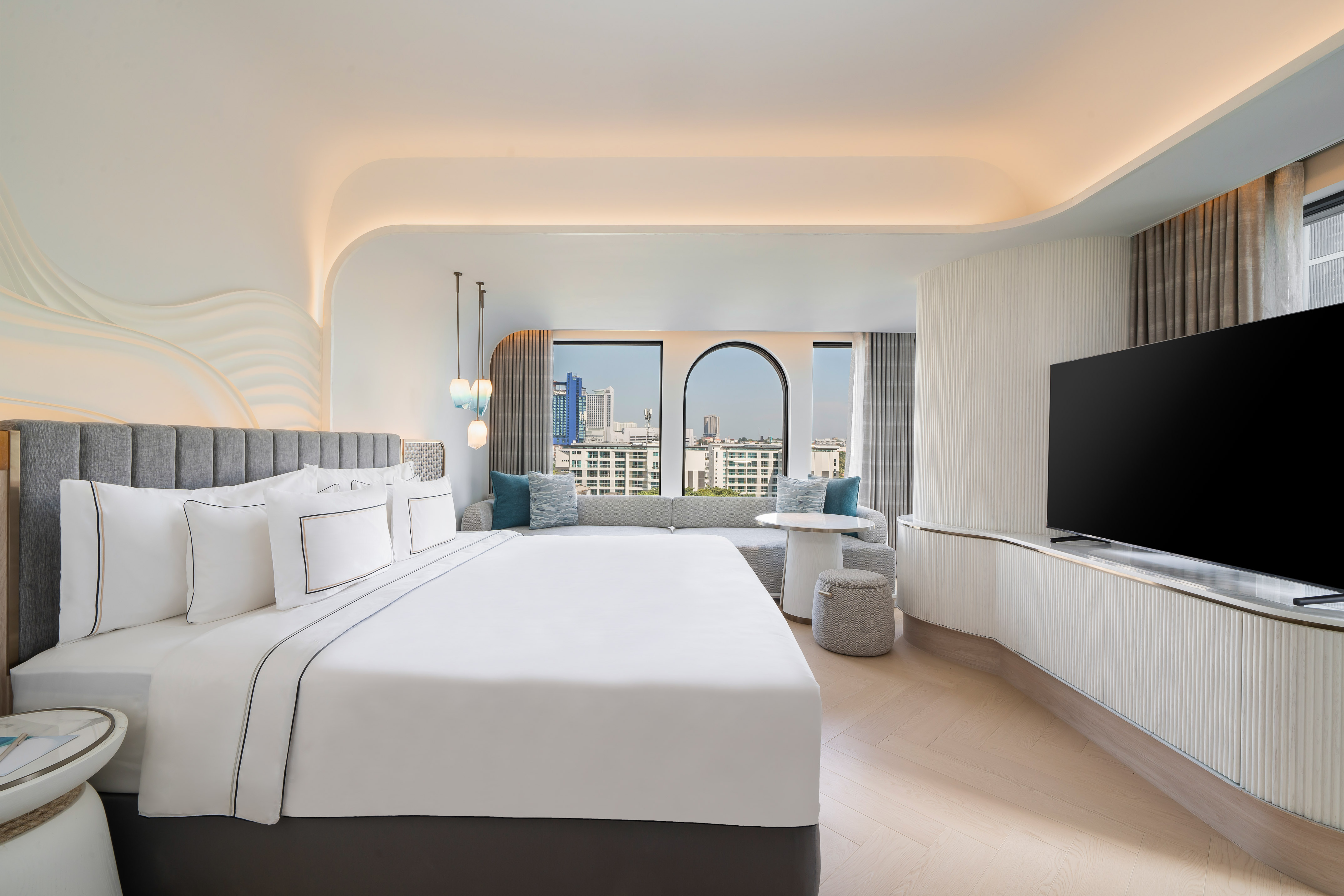 Modern hotel room with king bed, city view windows, and lounge area.