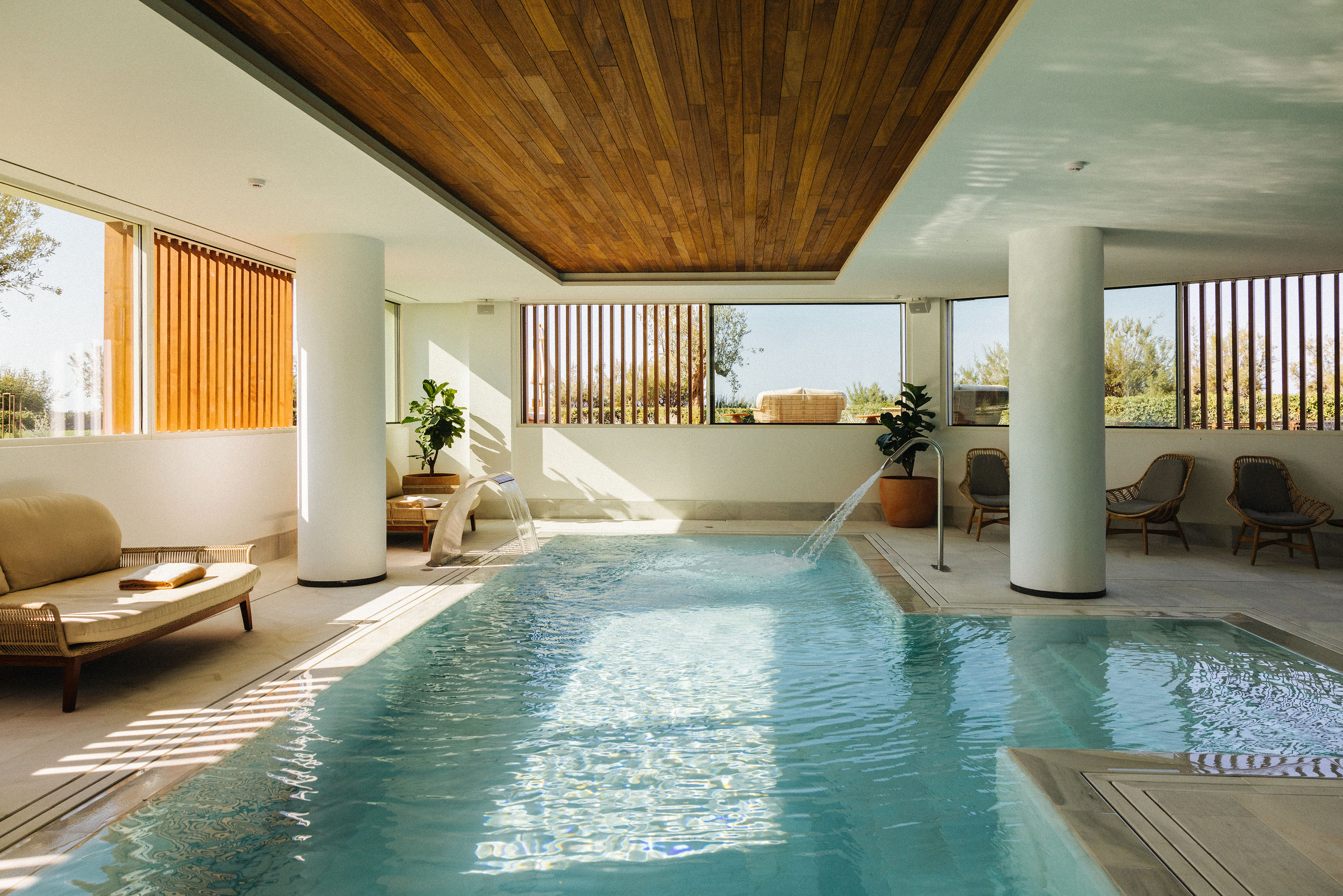 Modern indoor pool with wooden ceiling, sunlit windows, and spa lounge area.