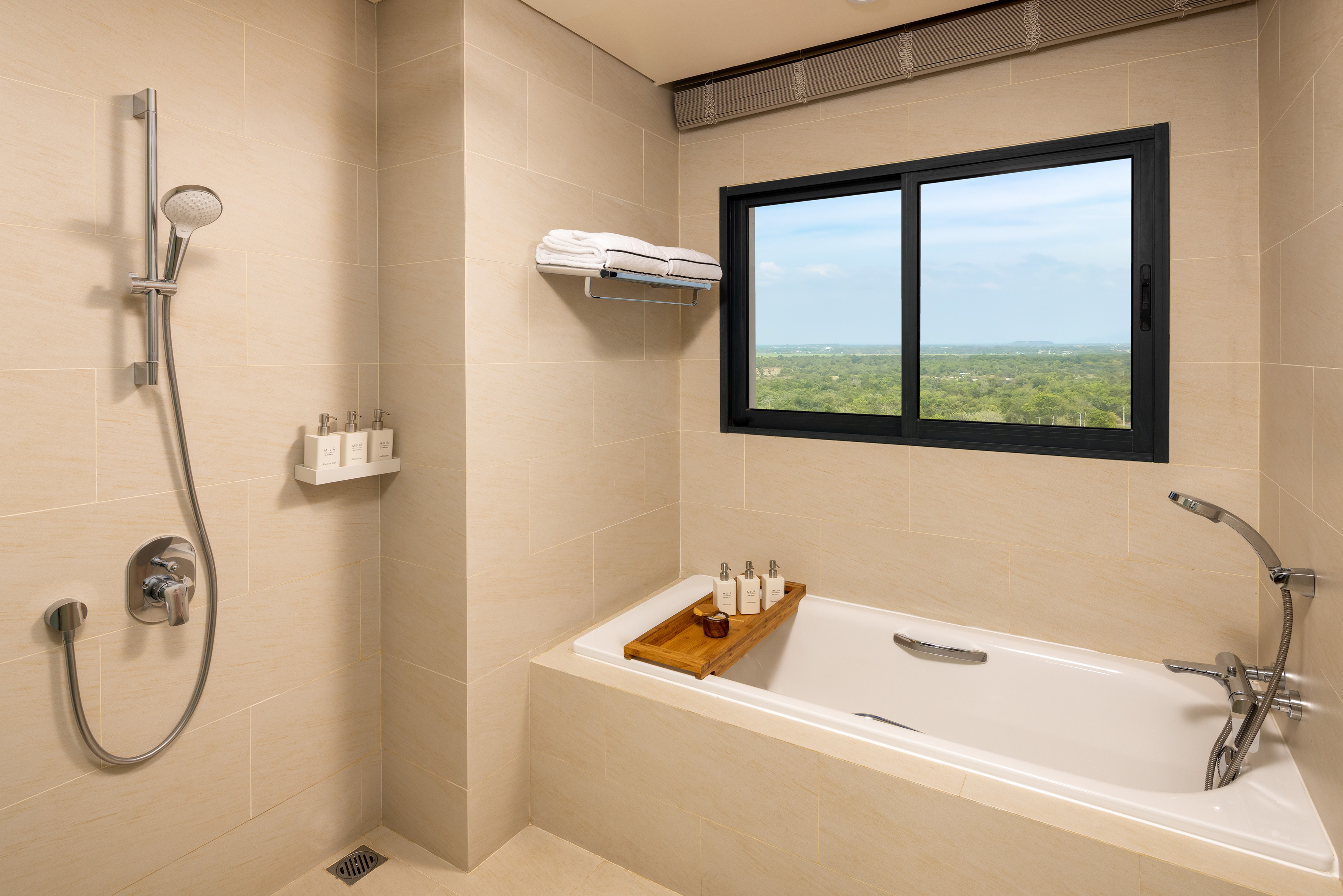 Modern hotel bathroom with shower, bathtub, beige tiles, and scenic window view.