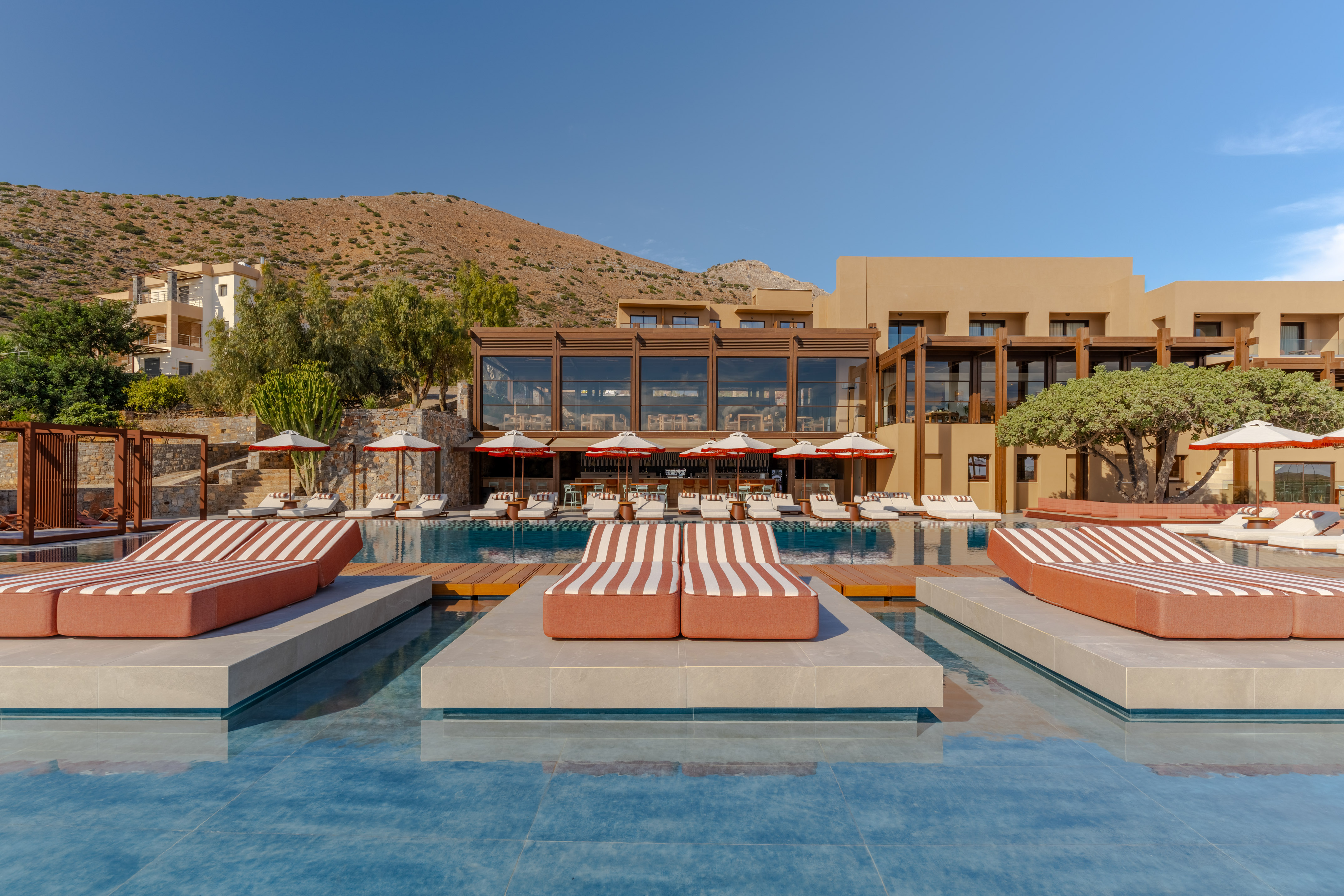 Luxury resort pool with striped daybeds, modern hotel, and mountain backdrop.