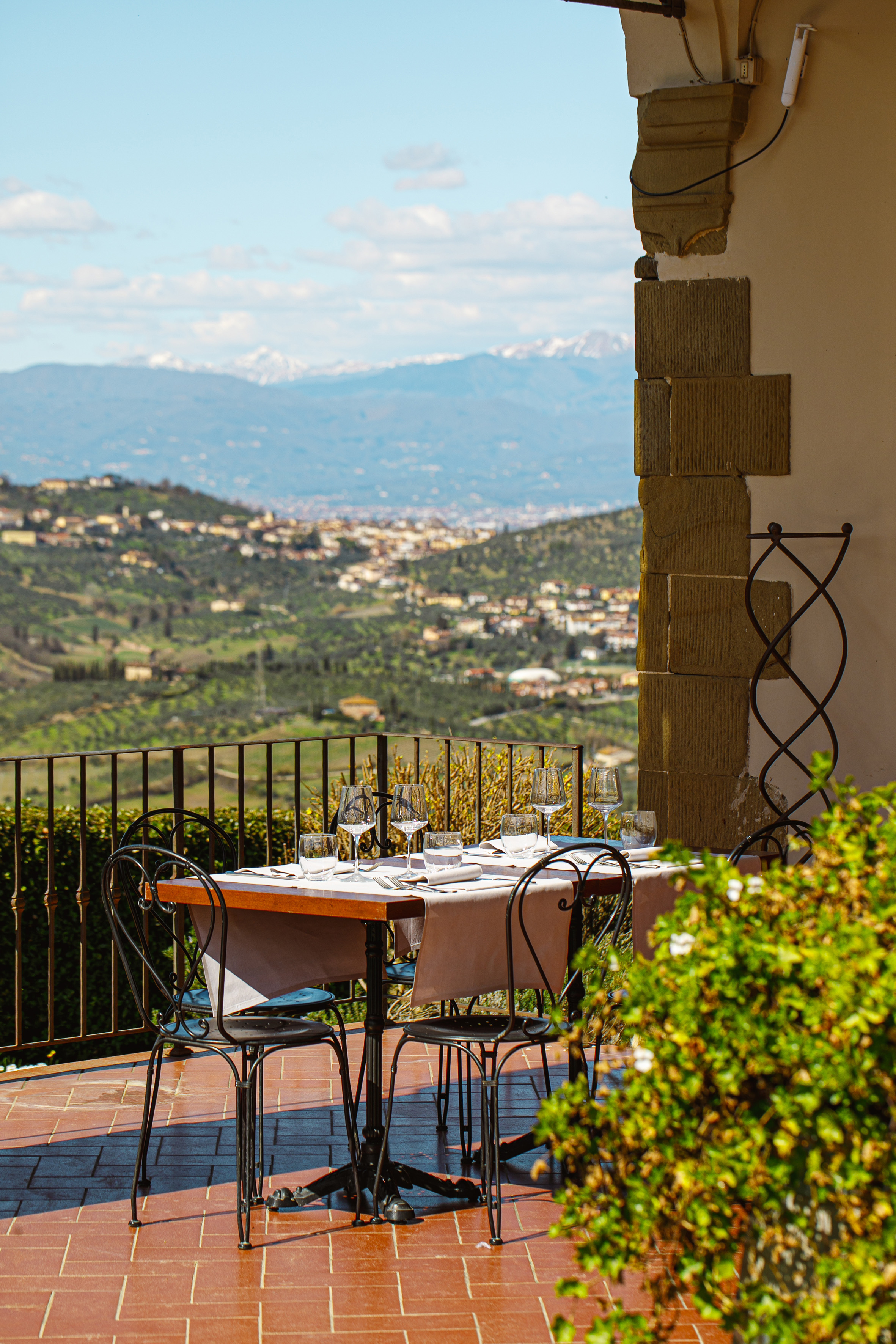 Outdoor dining table on terrace overlooking Tuscan valley and distant mountains.
