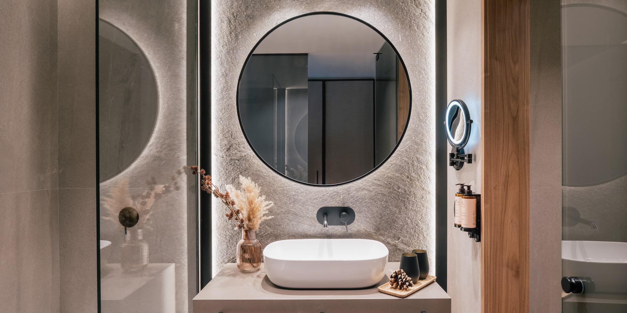 Contemporary bathroom with backlit round mirror, vessel sink, and stone wall.