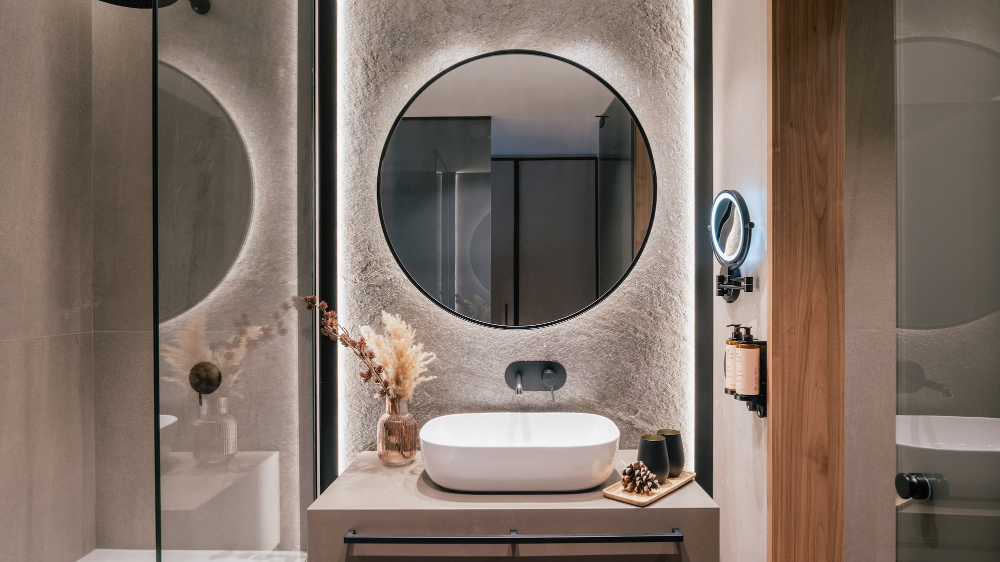 Contemporary bathroom with backlit round mirror, vessel sink, and stone wall.