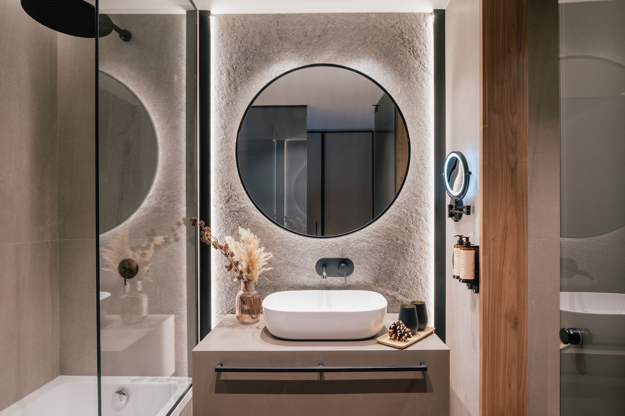Contemporary bathroom with backlit round mirror, vessel sink, and stone wall.