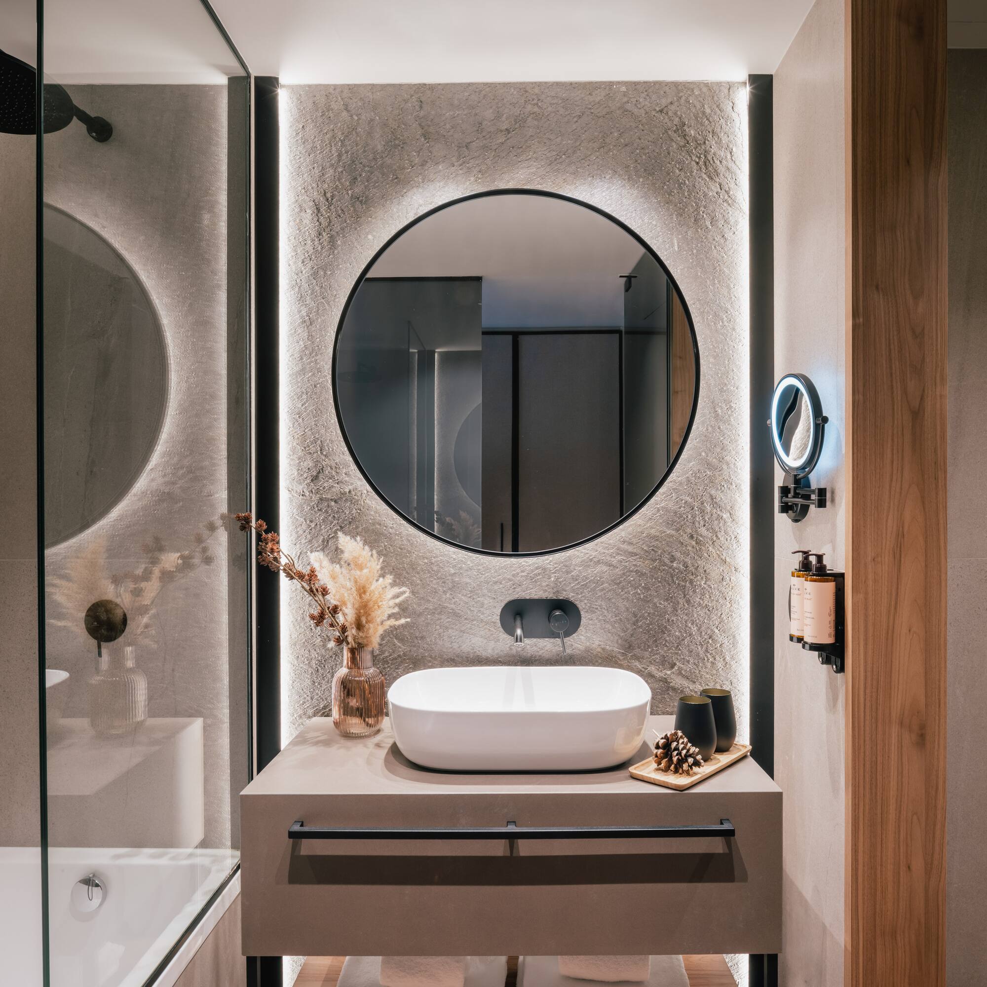 Contemporary bathroom with backlit round mirror, vessel sink, and stone wall.