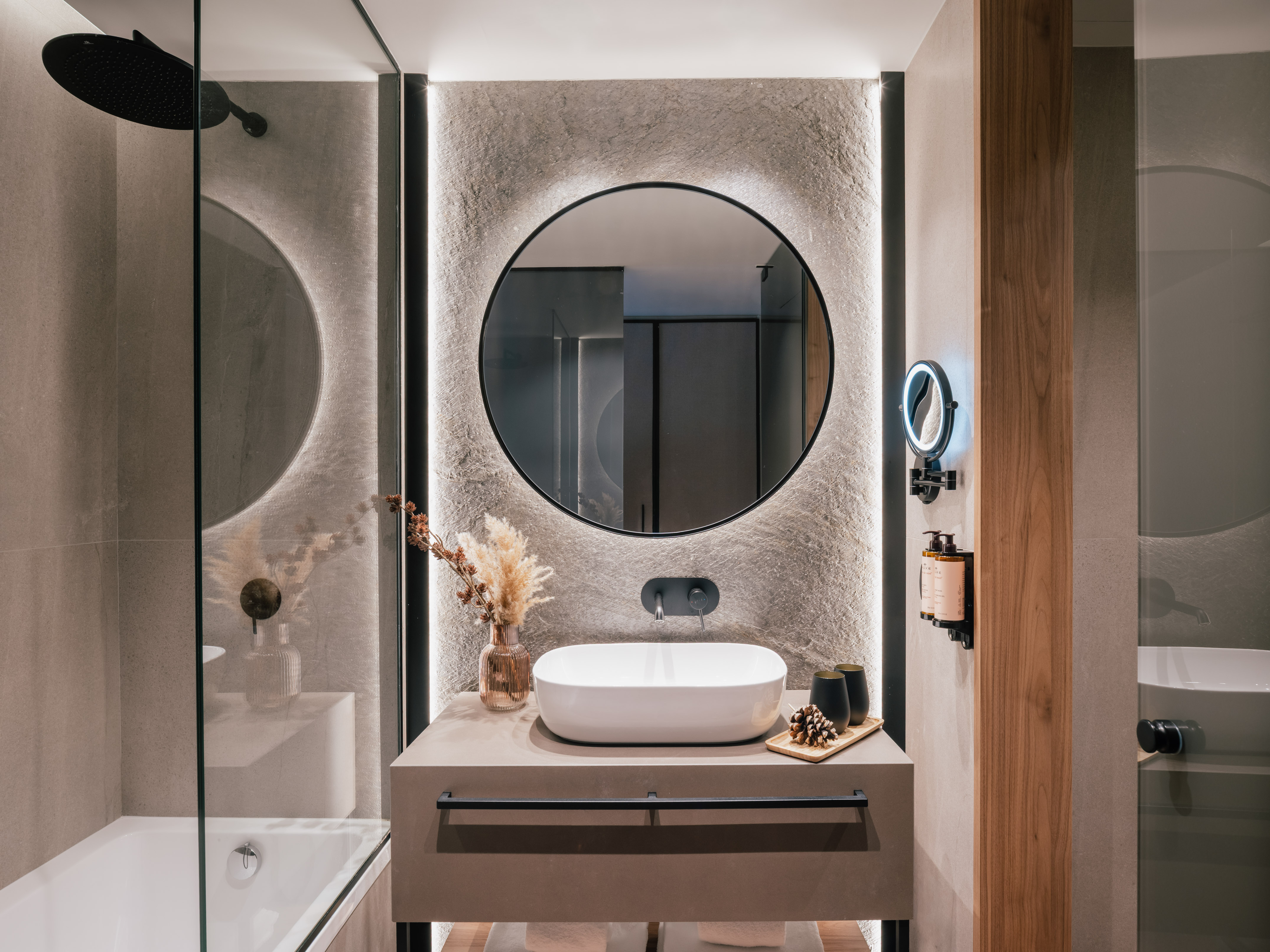 Contemporary bathroom with backlit round mirror, vessel sink, and stone wall.