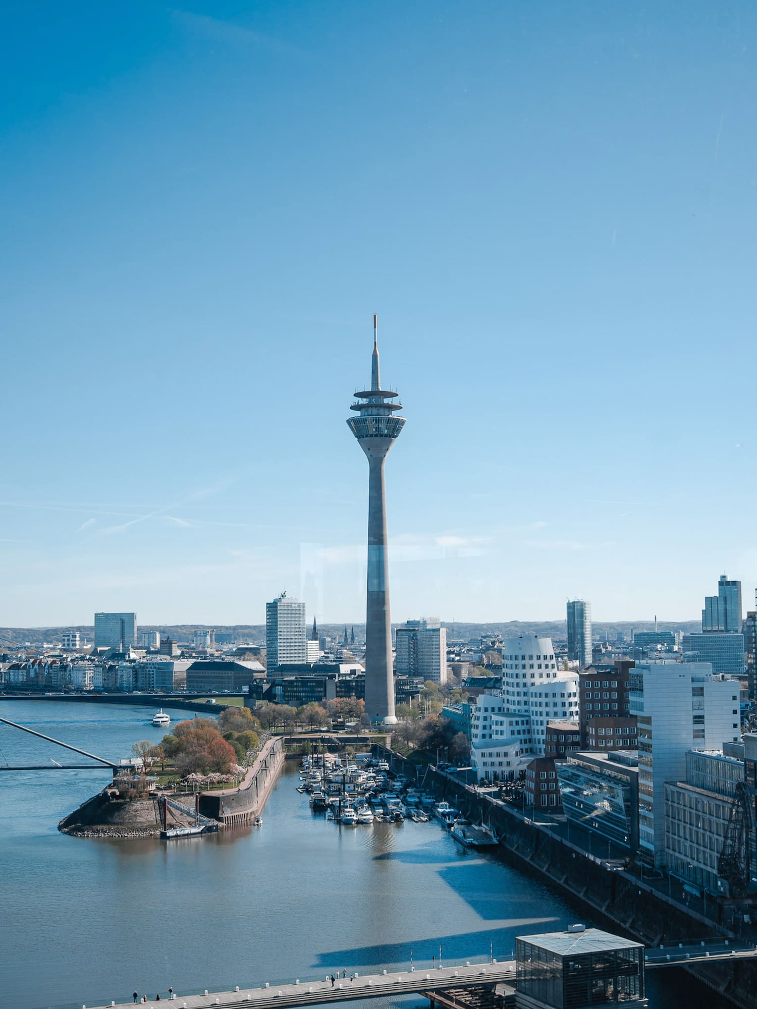 Düsseldorf skyline with Rheinturm, Rhine river, and marina under blue sky.