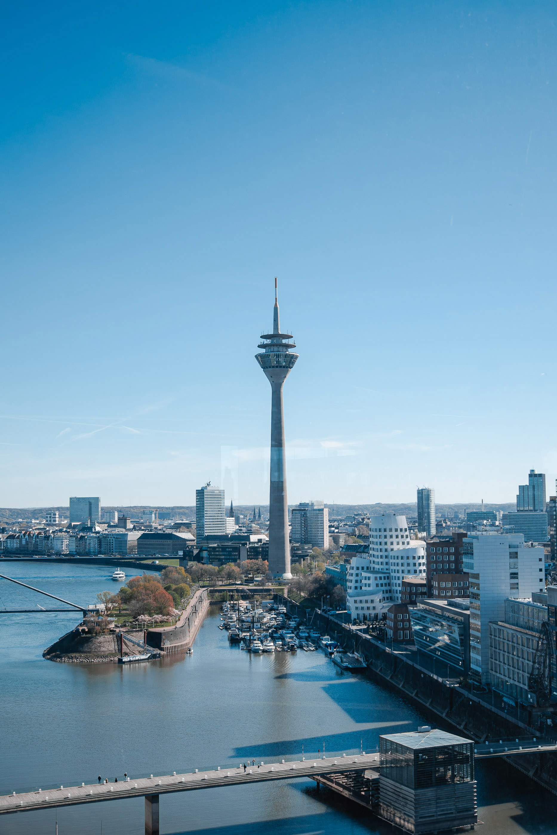 Düsseldorf skyline with Rheinturm, Rhine river, and marina under blue sky.