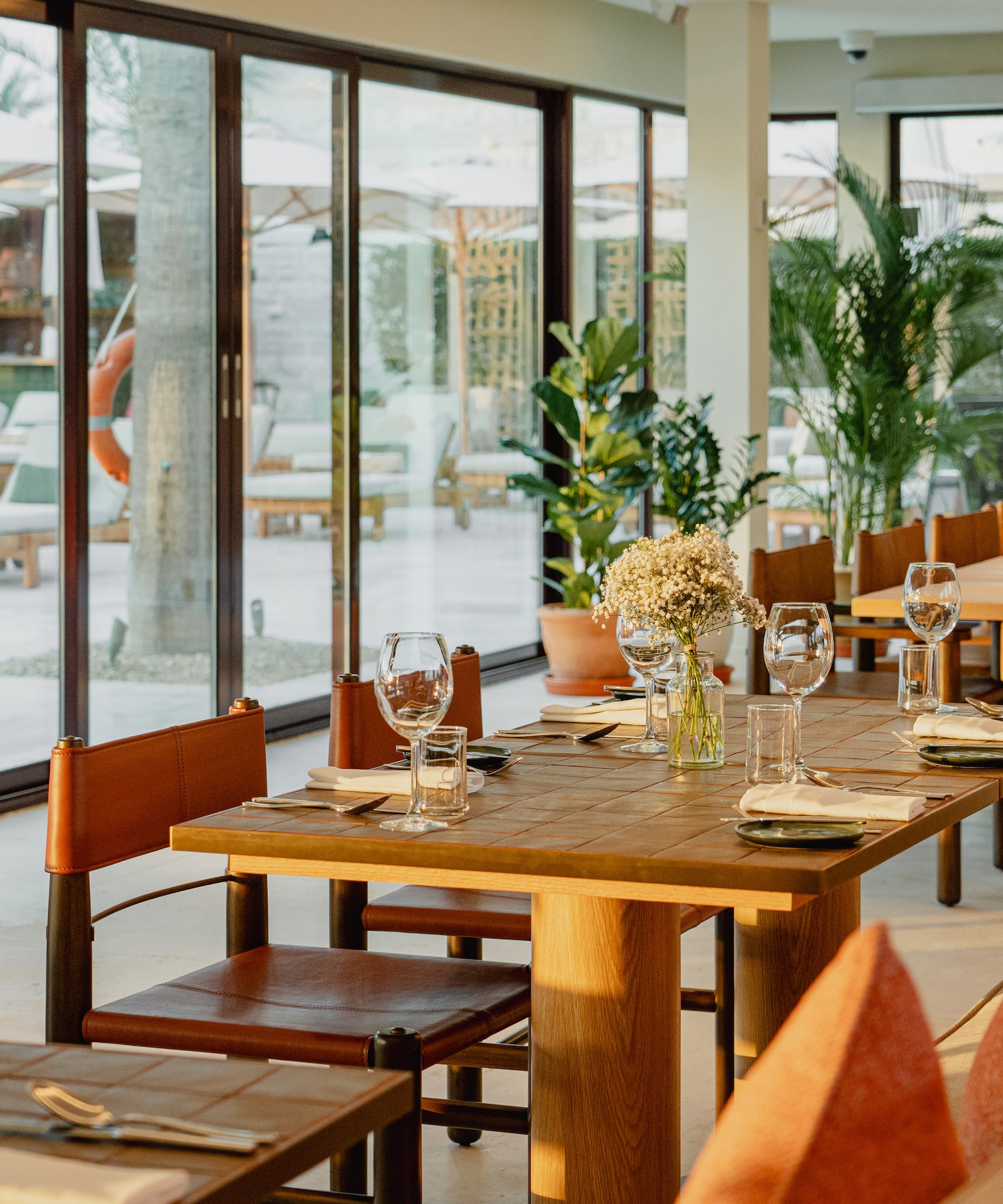 Sunny restaurant dining area with set tables, leather chairs, and patio view.