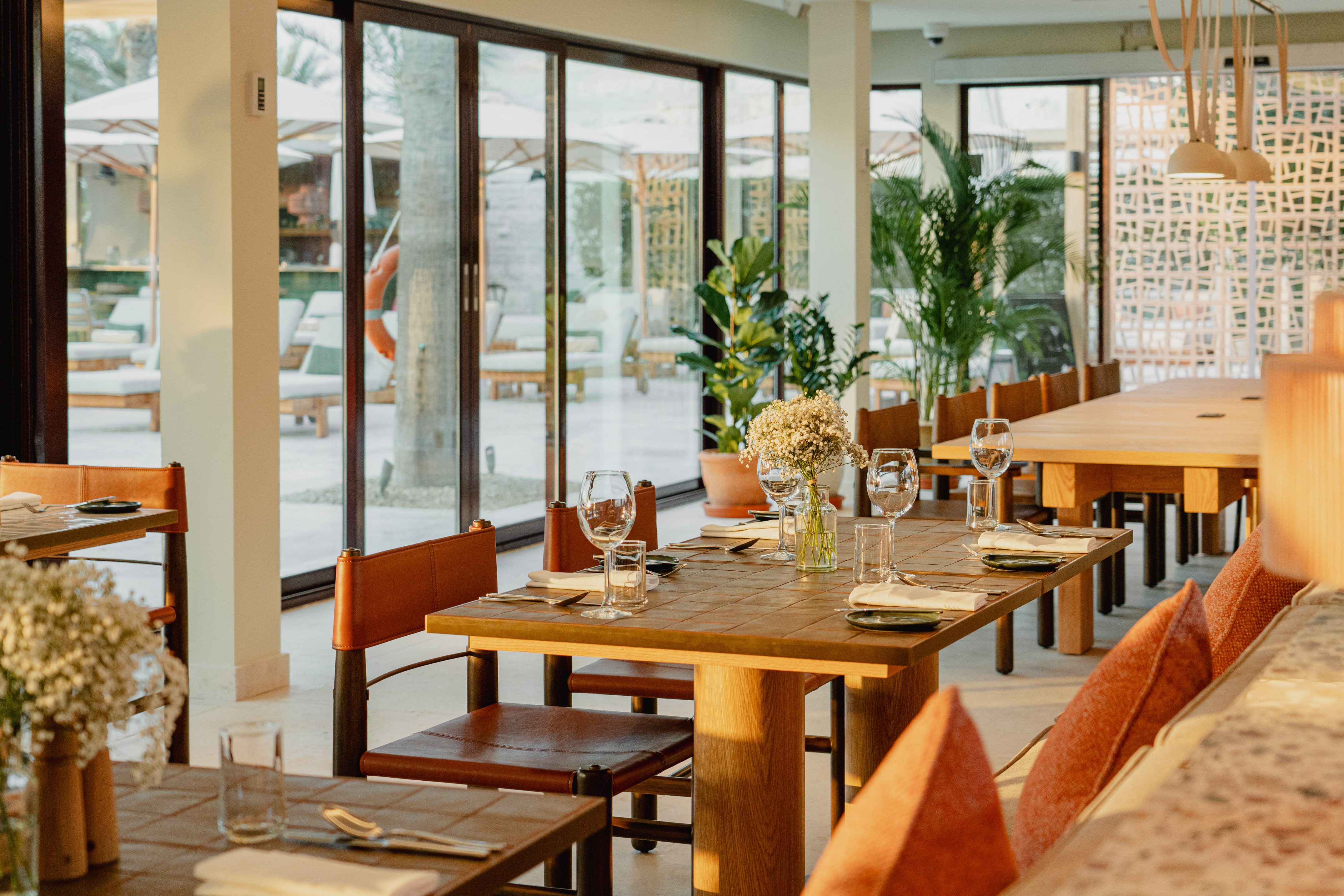 Sunny restaurant dining area with set tables, leather chairs, and patio view.