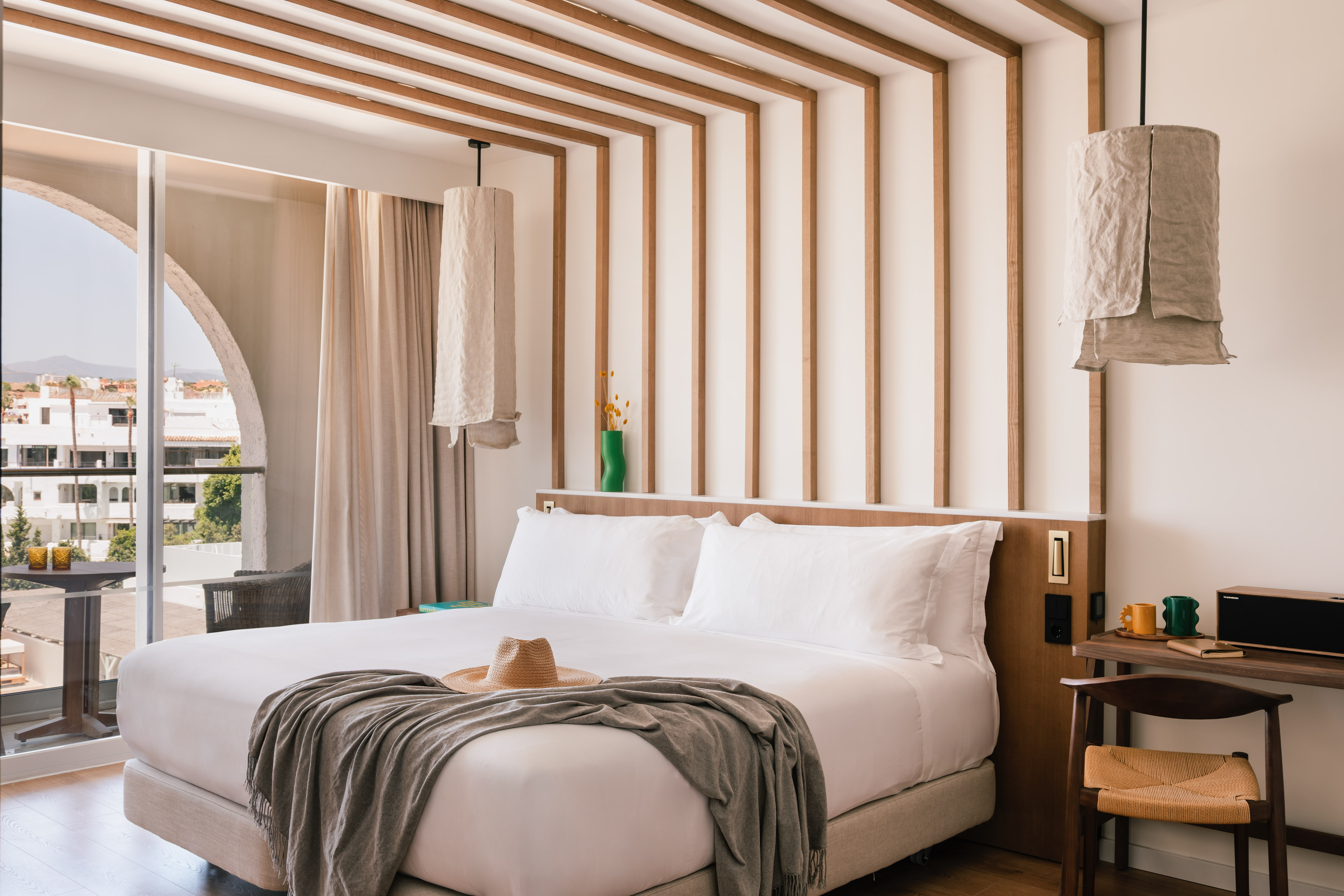 Modern hotel bedroom with wooden slatted decor, white bed, and balcony view.