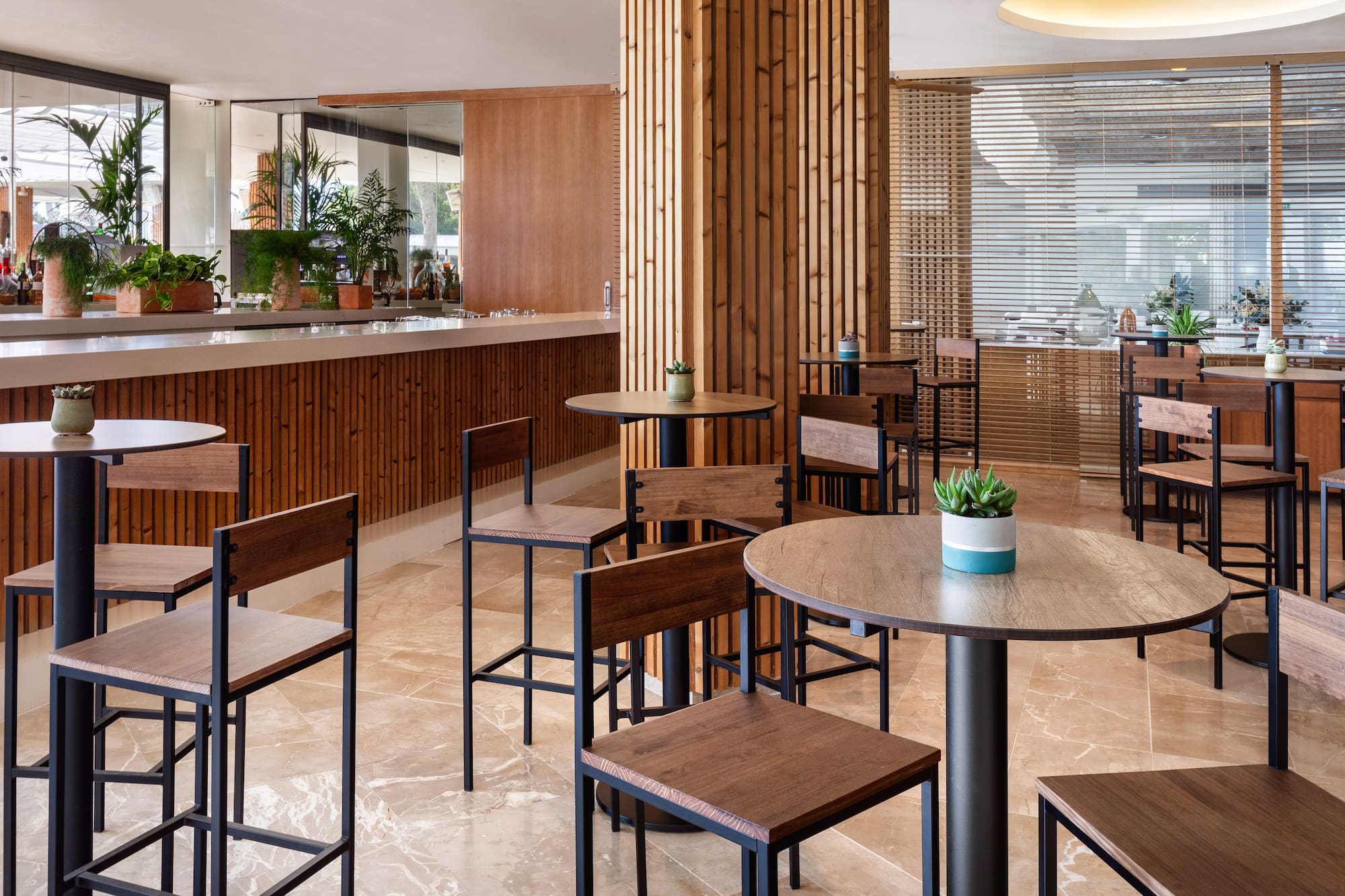 Hotel bar interior: wood paneling, high tables, dark bar stools, plants.