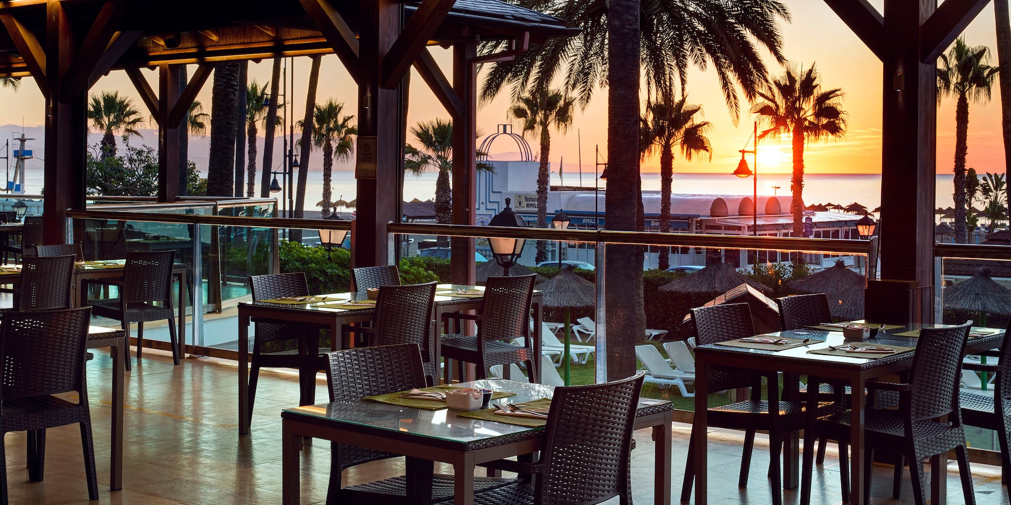 Tropical resort dining terrace with ocean sunset and palm trees.