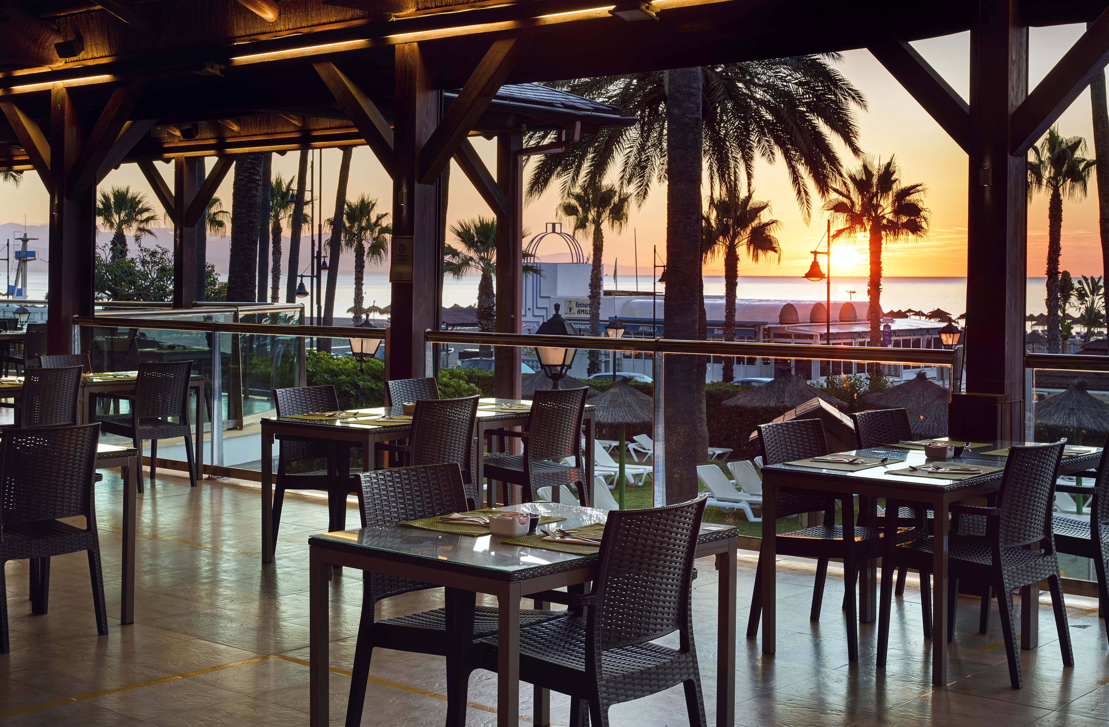 Tropical resort dining terrace with ocean sunset and palm trees.