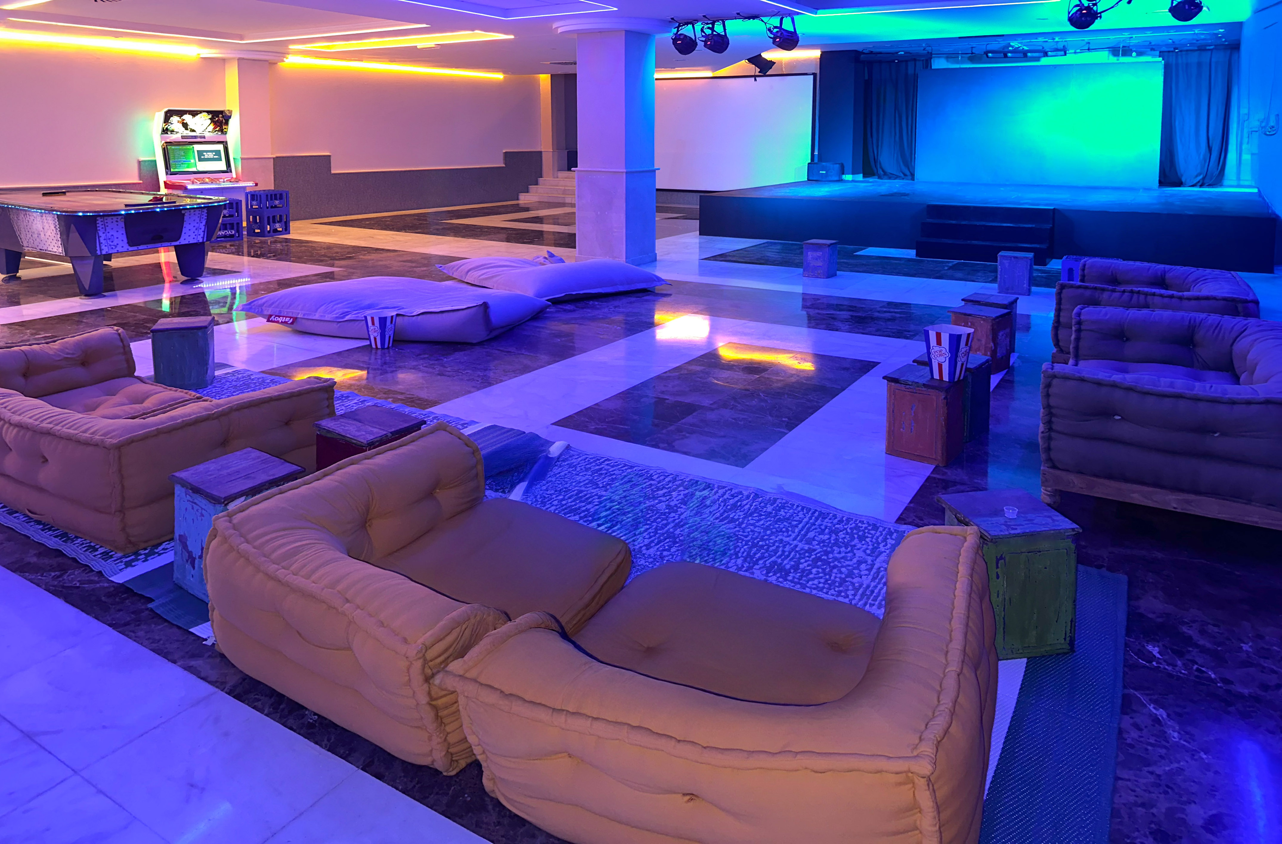 Vibrant entertainment lounge with stage, gaming, modular seating, neon lighting.