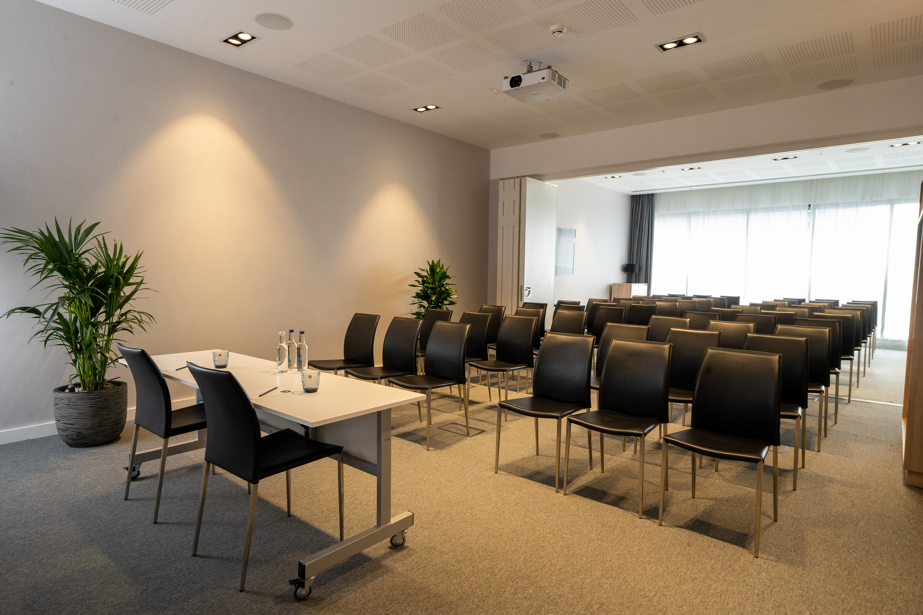 Modern conference room with rows of black chairs, projector, and meeting table.