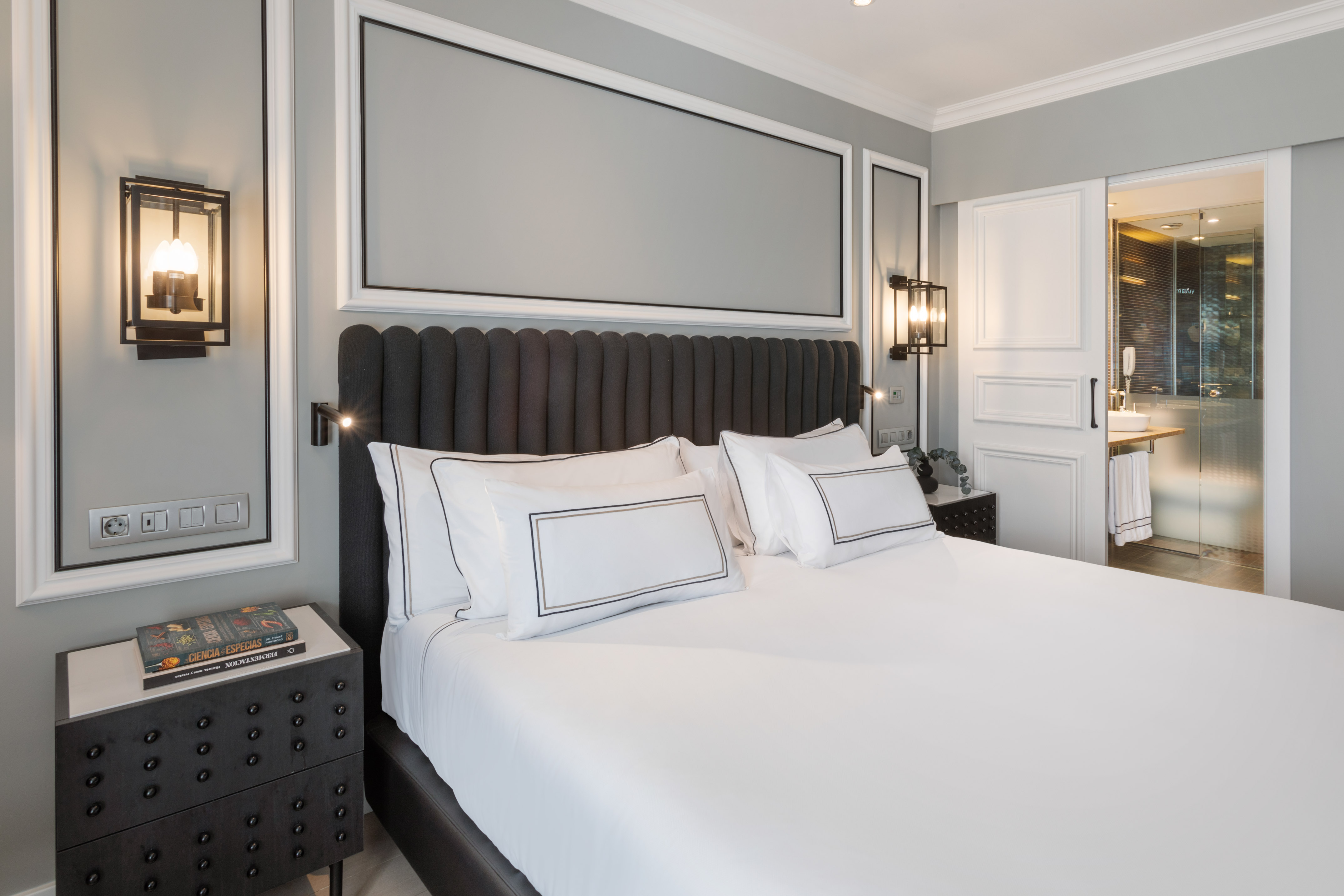 Stylish hotel bedroom with gray headboard, white bed, and elegant sconces.