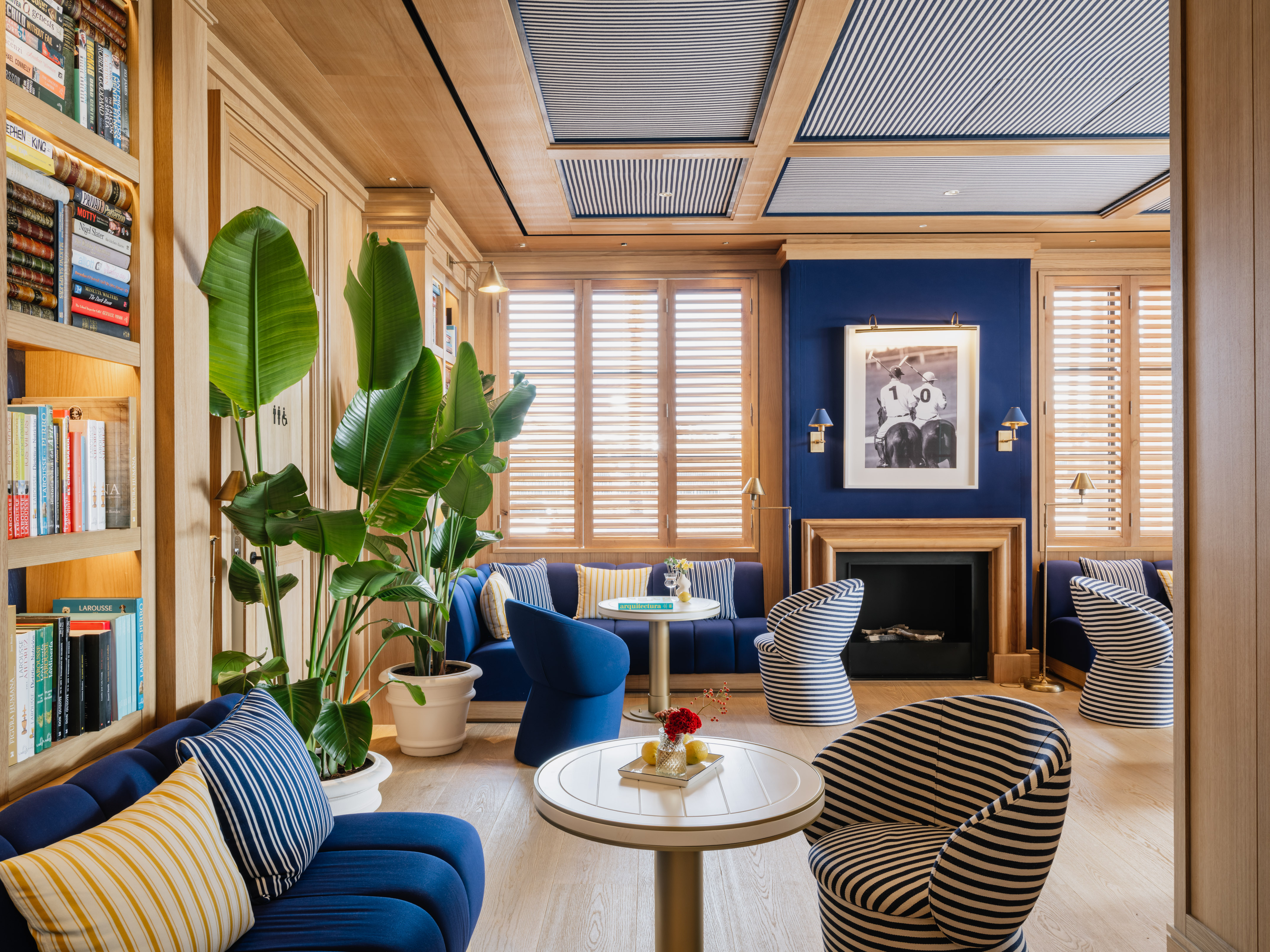 Navy and wood luxury lounge with striped chairs, bookshelves, and fireplace.