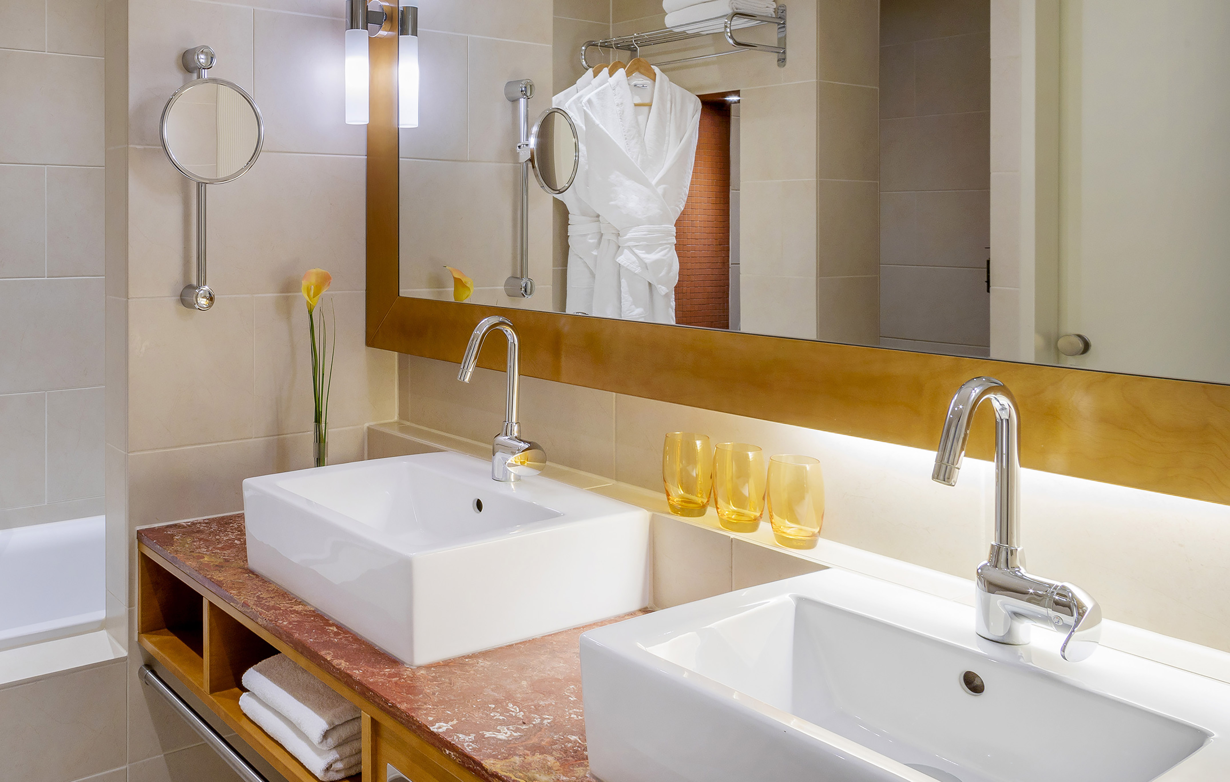 Modern bathroom with dual sinks, marble vanity, large mirror, and bathrobes.