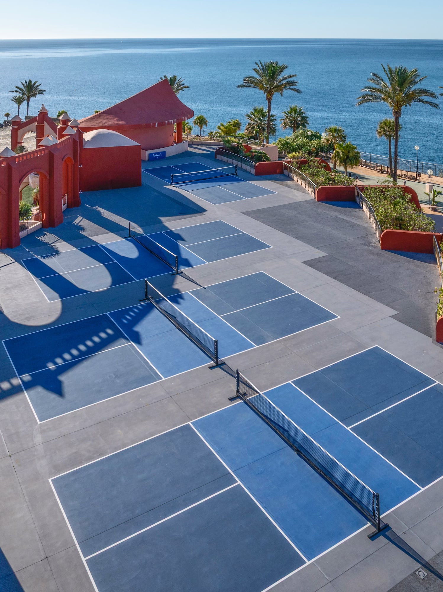 Outdoor pickleball courts at a coastal resort with ocean view and palm trees.