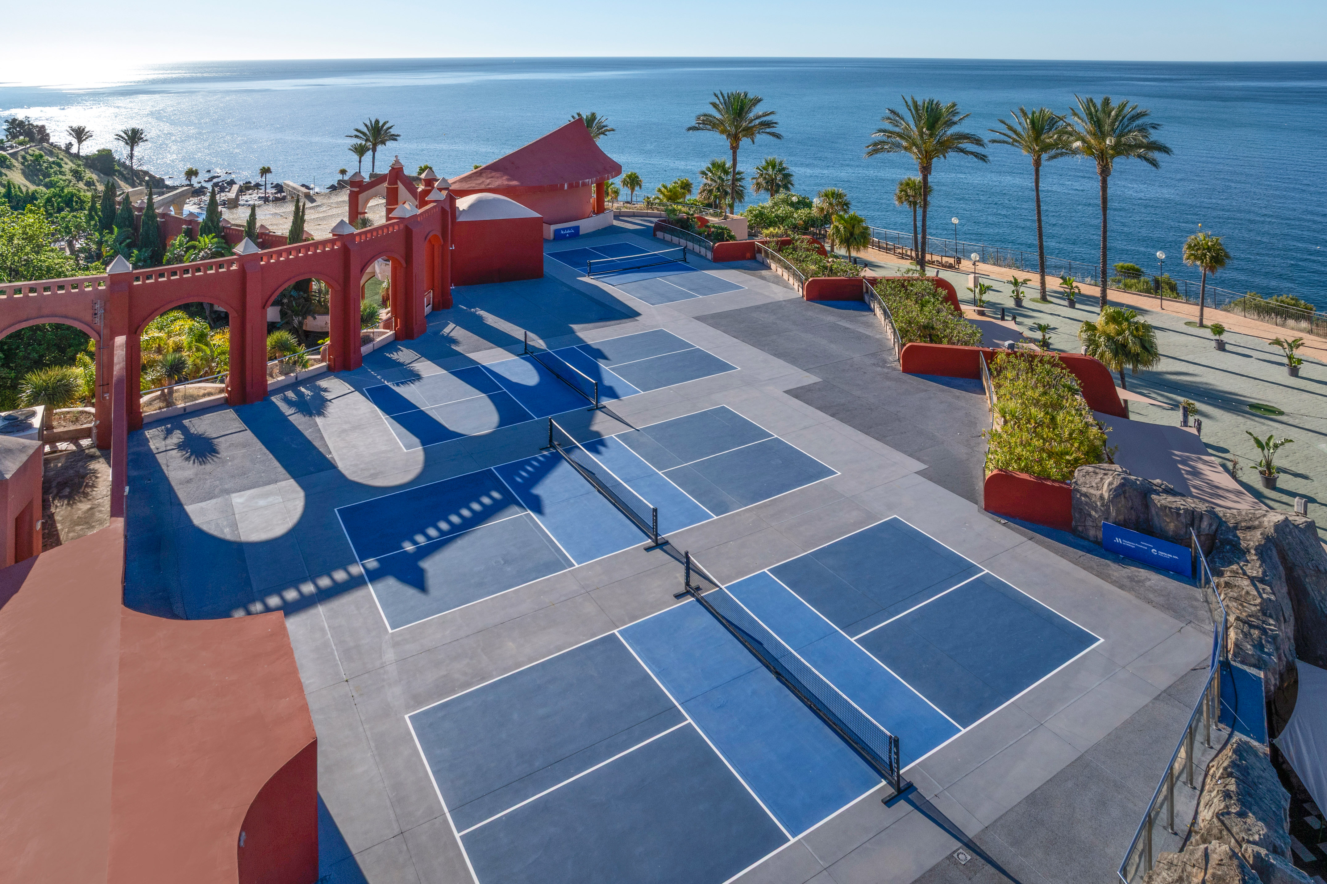 Outdoor pickleball courts at a coastal resort with ocean view and palm trees.