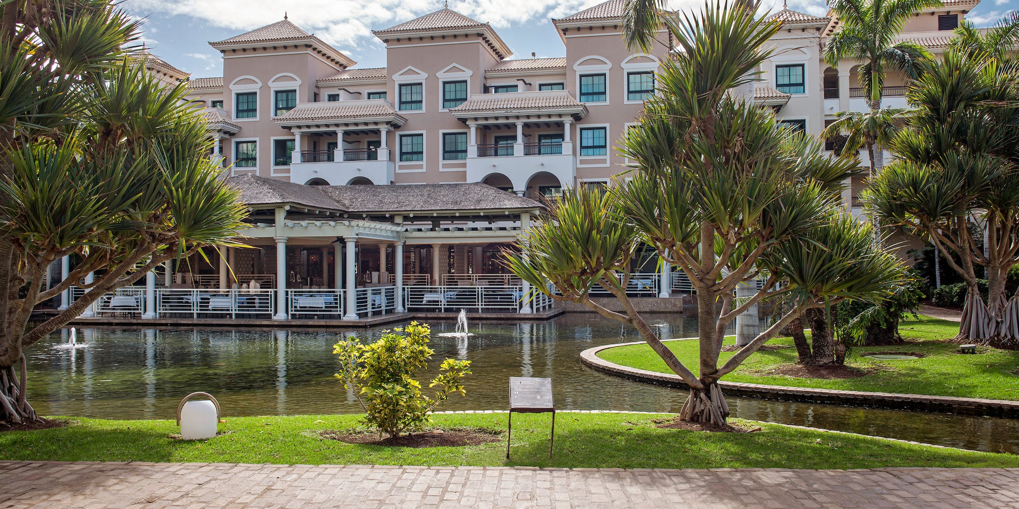 Mediterranean resort with tropical gardens, reflective pond, and palm trees.