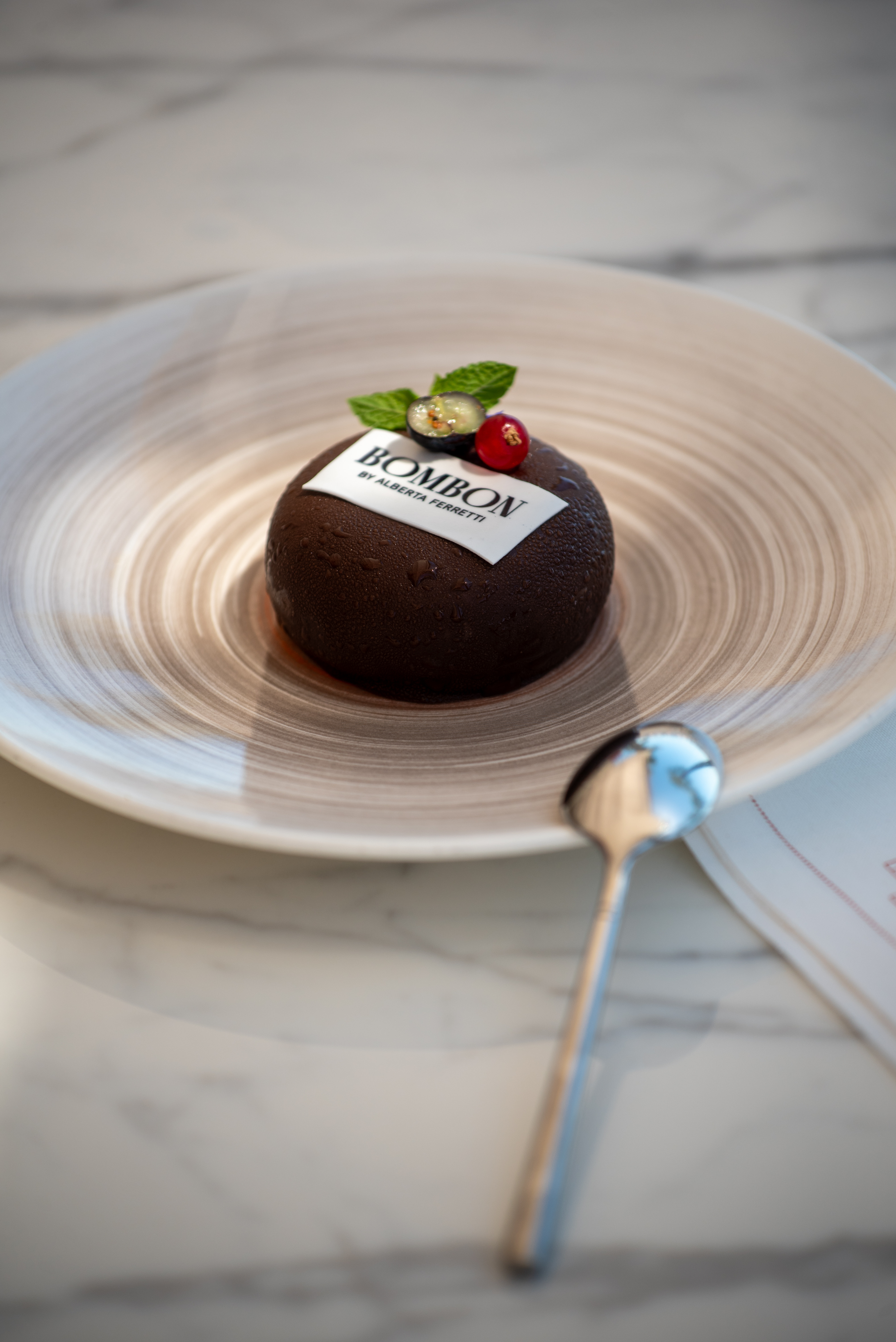 Dark chocolate Bombon dessert by Alberta Ferretti, topped with berries and mint.