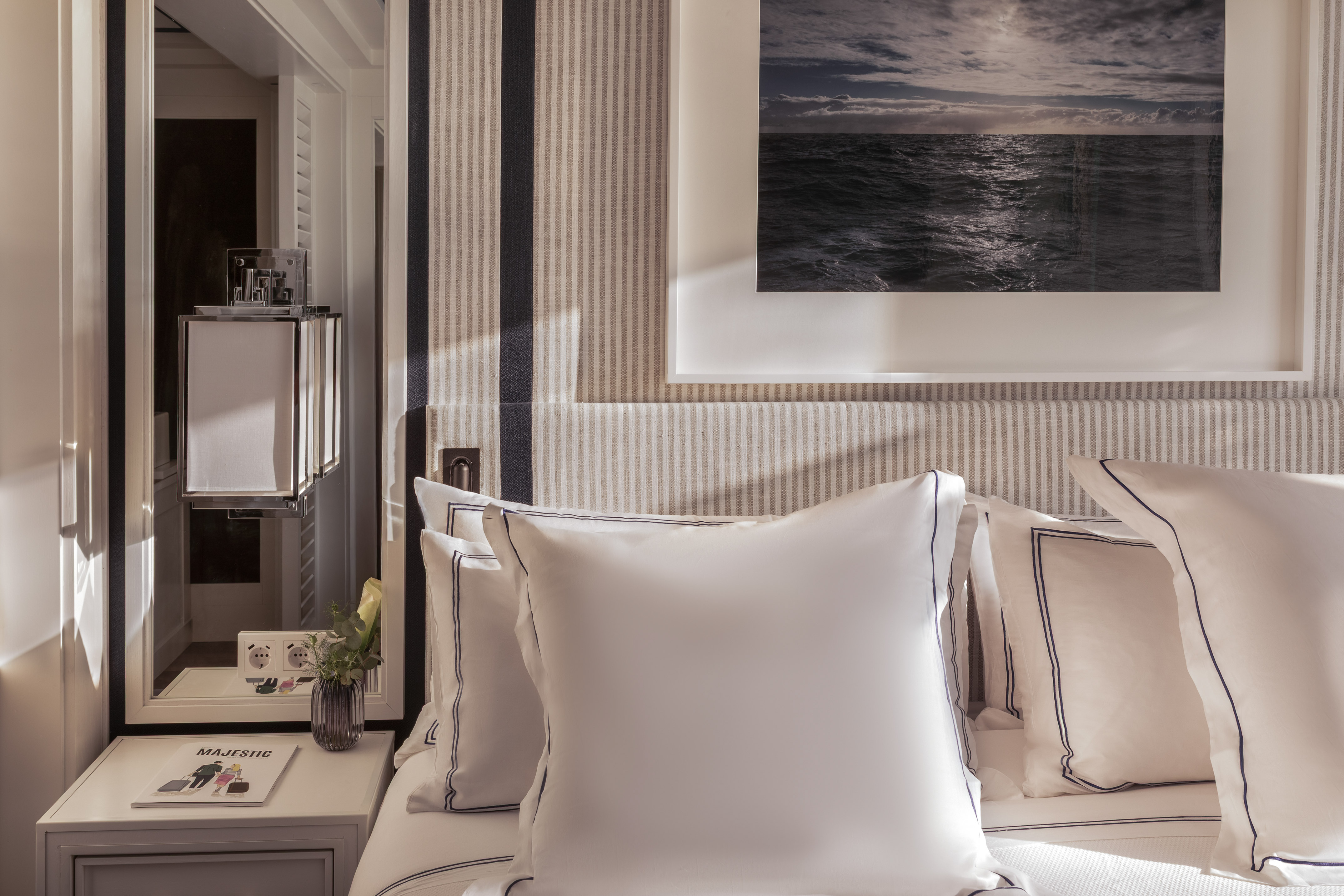 Stylish bedroom with striped headboard, white bedding, and ocean artwork.