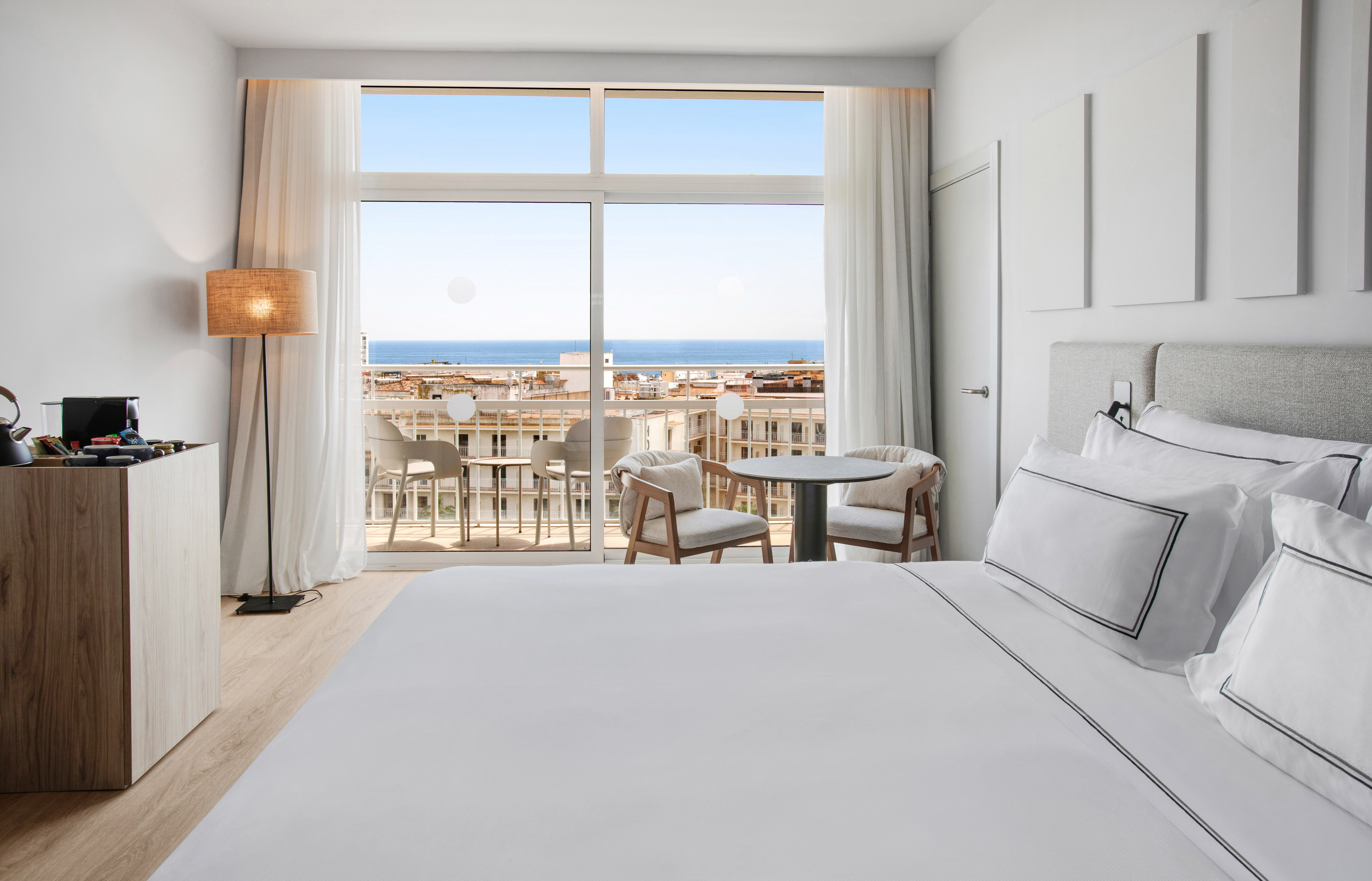 Modern hotel room with king bed, balcony sea view, and outdoor seating.