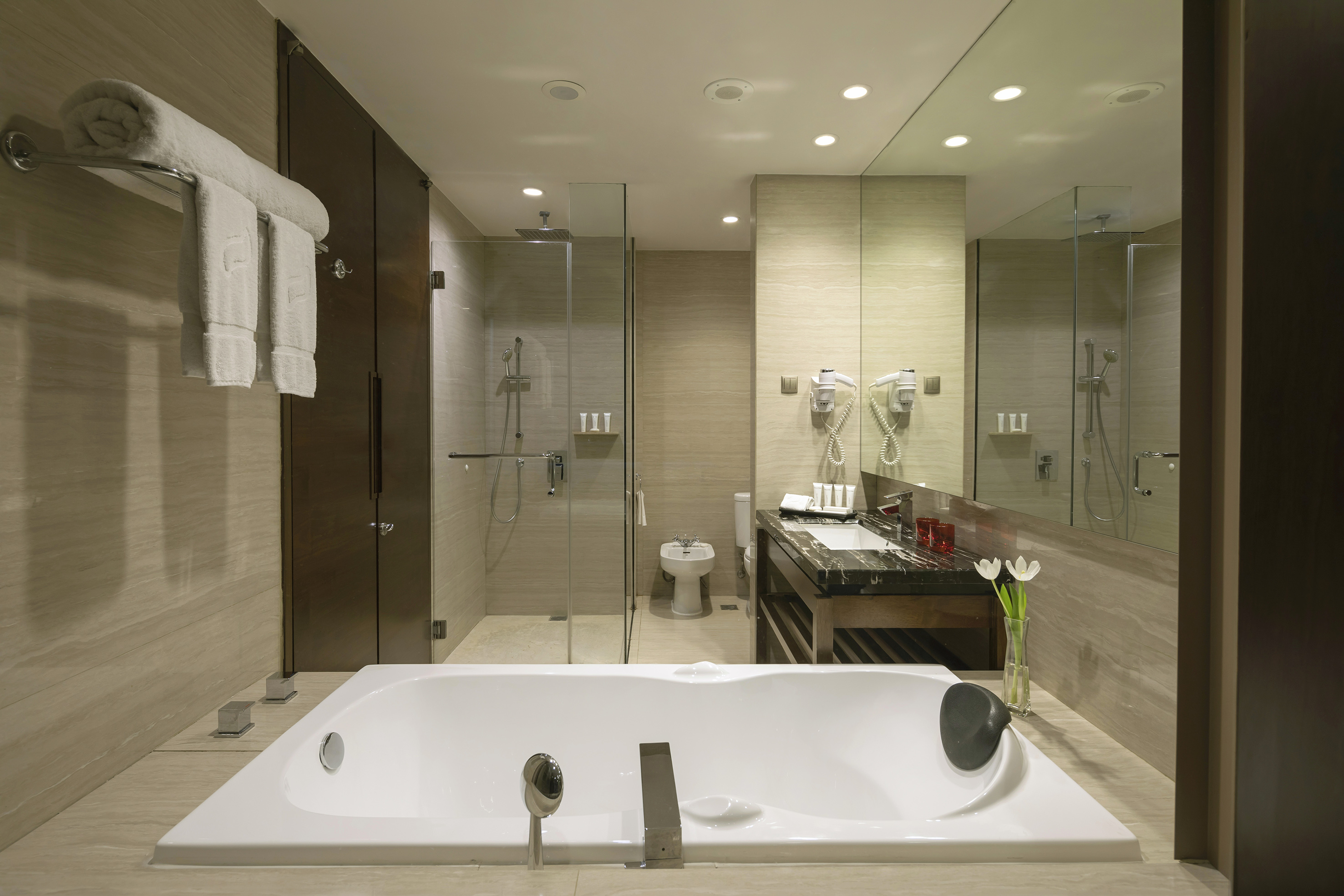 Modern hotel bathroom with large bathtub, glass shower, and stone vanity.